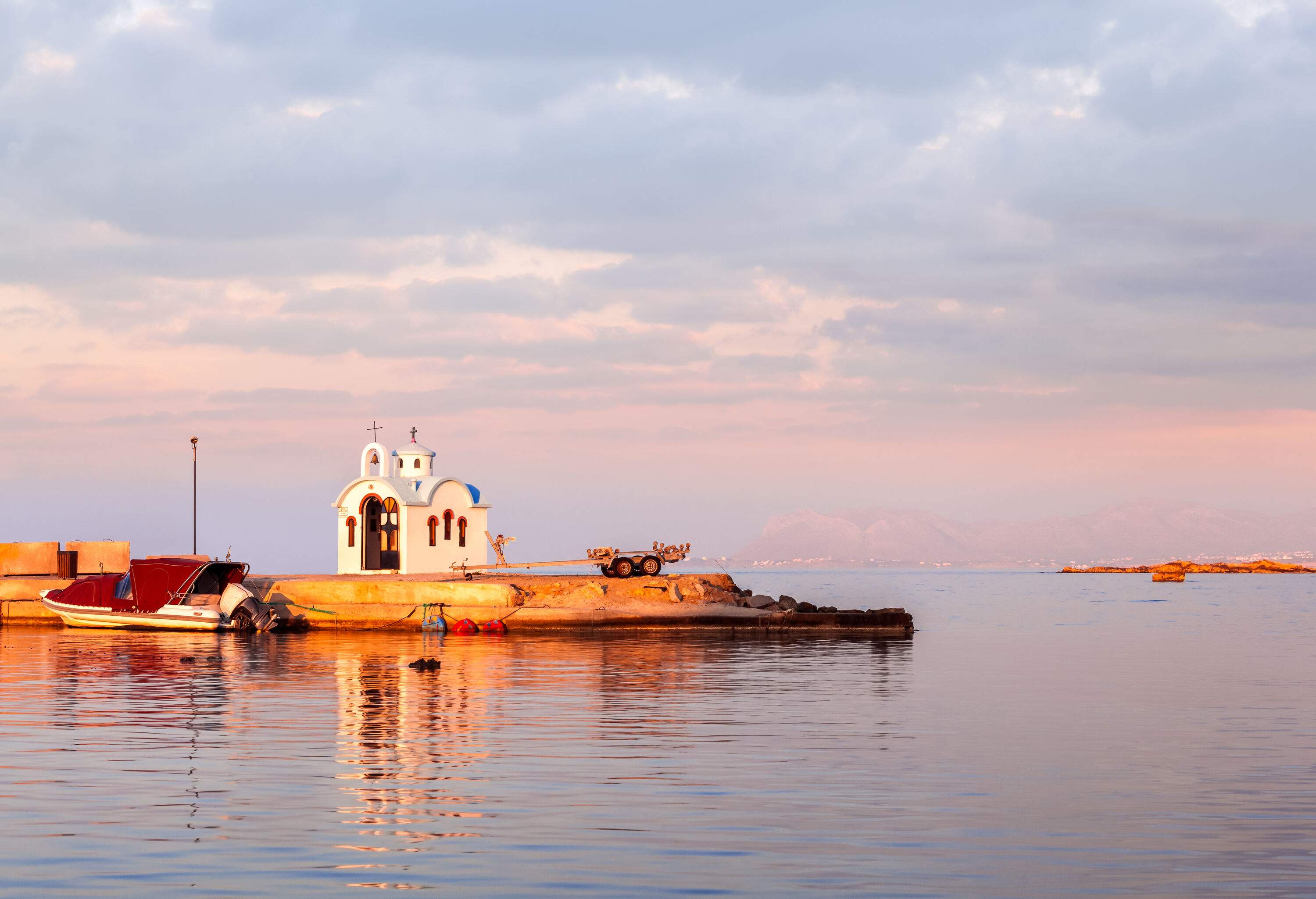 A white traditional Greece chapel on a rock island by the sea against the twilight sky.