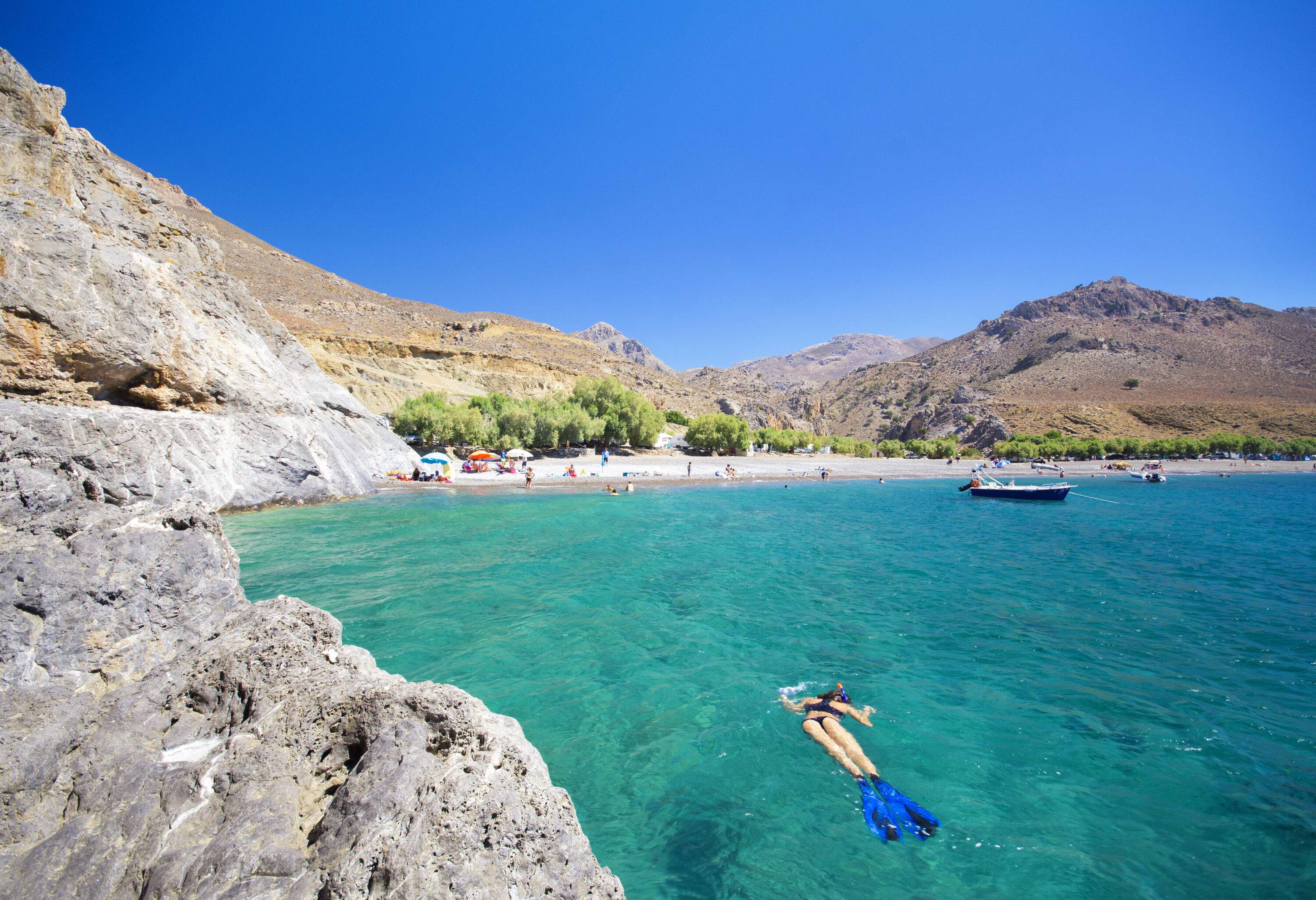 A person snorkeling in turquoise water surrounded by rocky mountains.