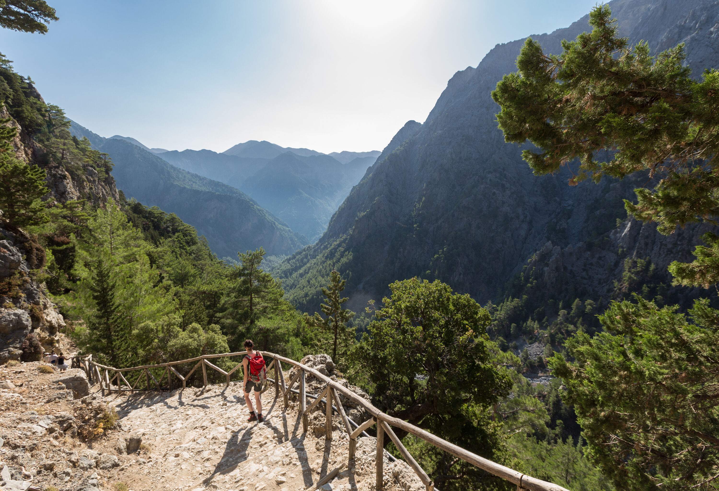 A female hiker descending a fenced trail in the mountains.