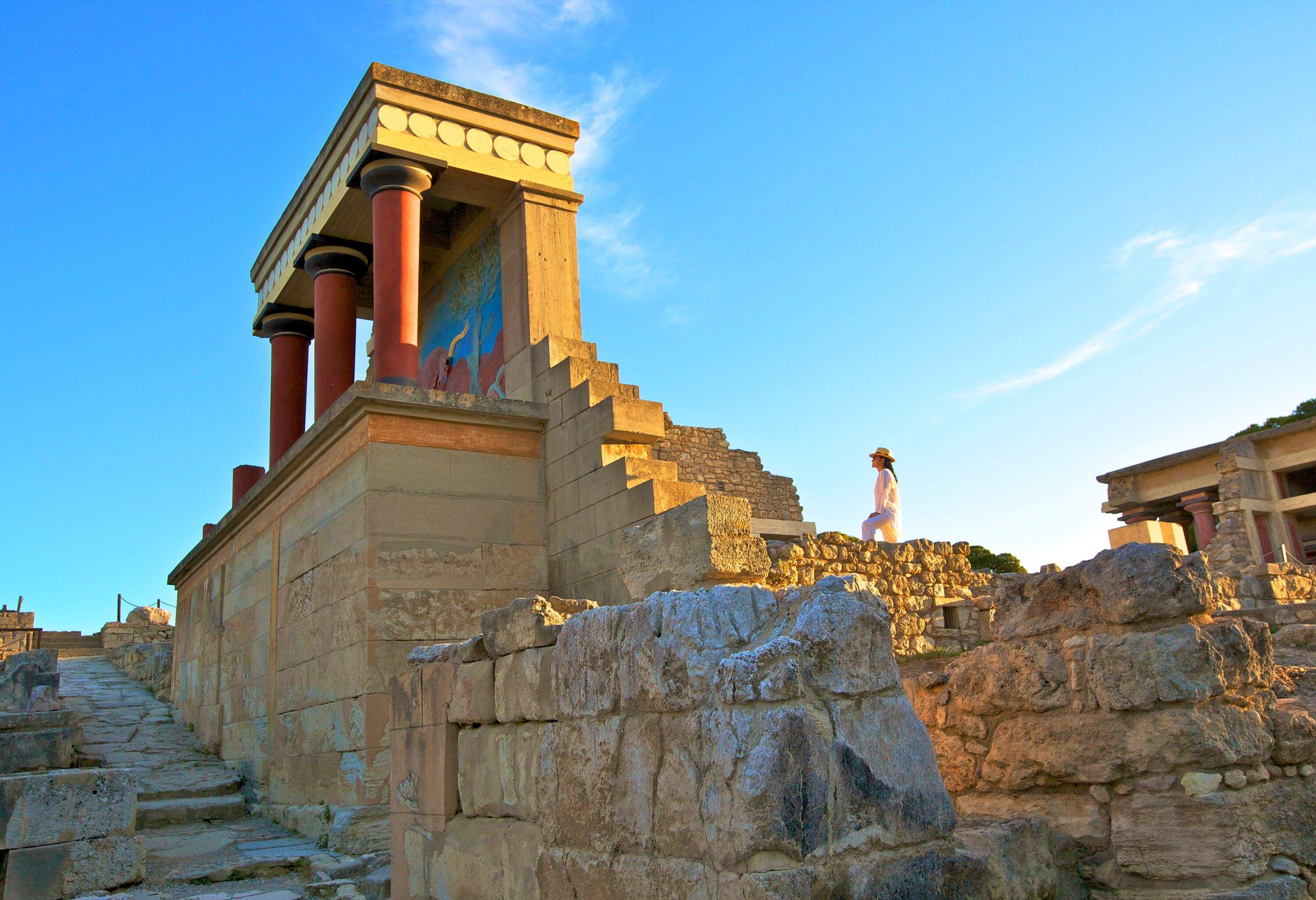 A person stares at a ruined palace's pillared porch made of piled stones.