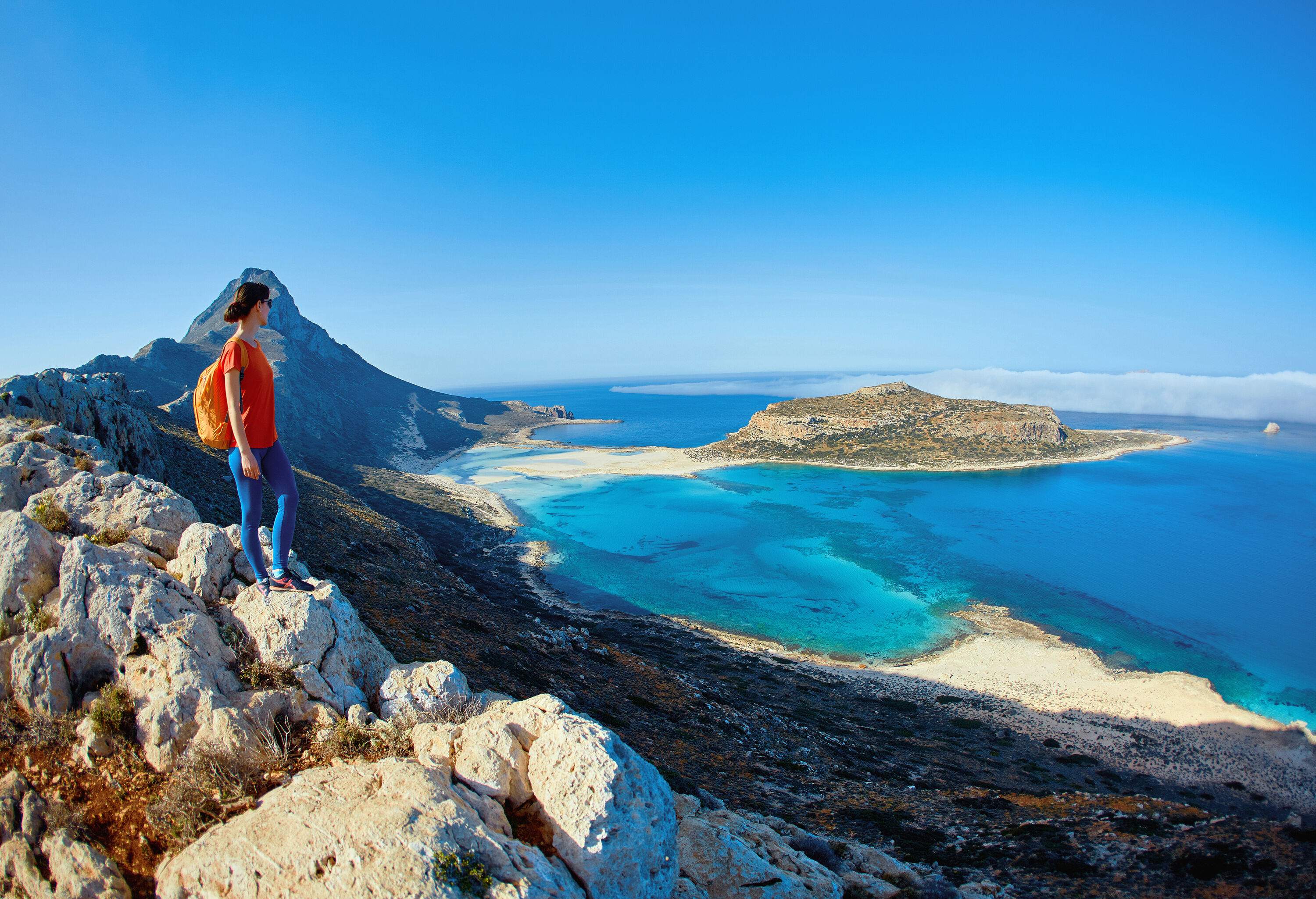 A woman standing on a rock admiring the natural beauty of the beach and turquoise waters.