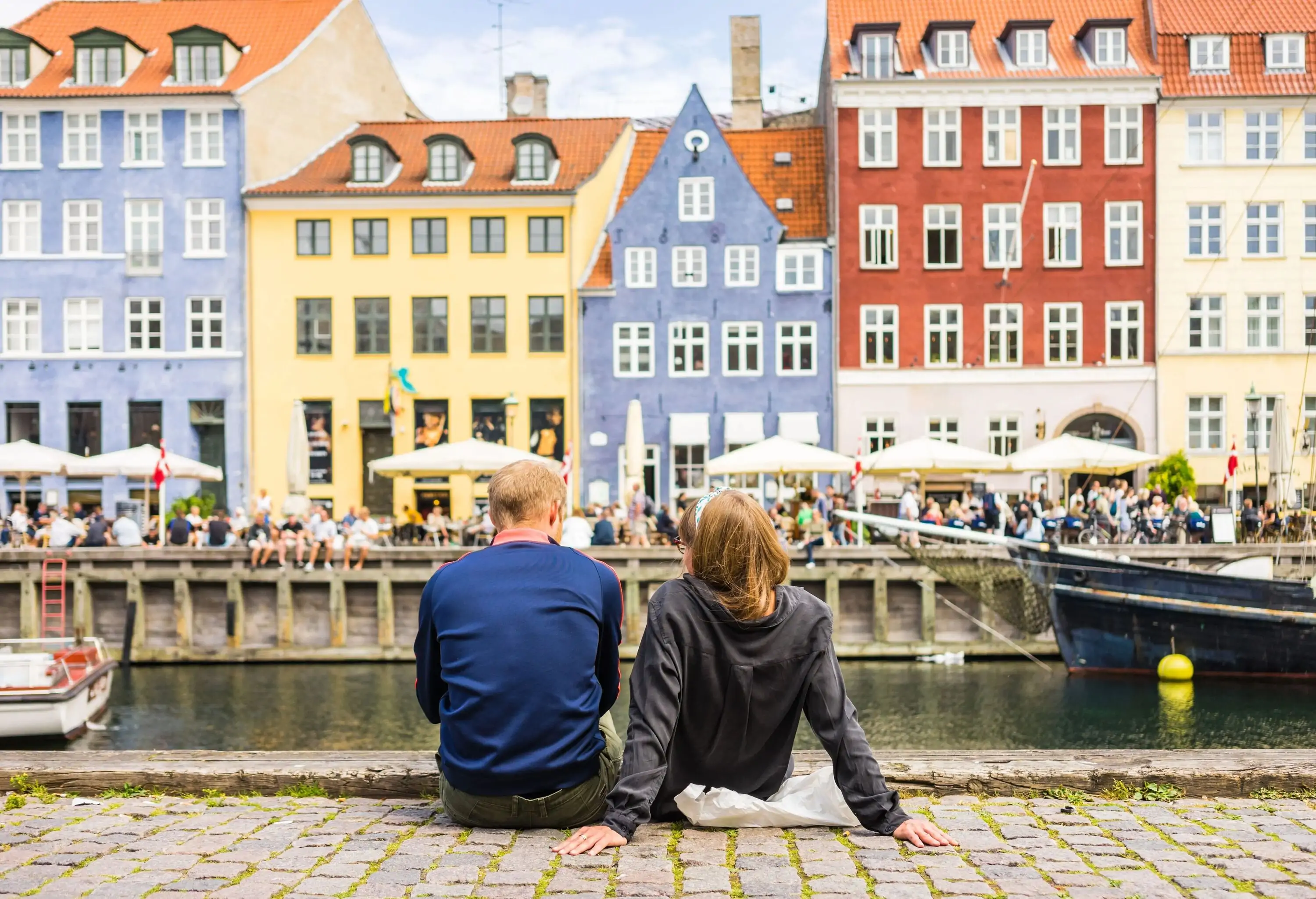 Couple enjoying the scenic summer view of Nyhavn pier. Colorful building facades with boats and yachts in the Old Town of Copenhagen, Denmark