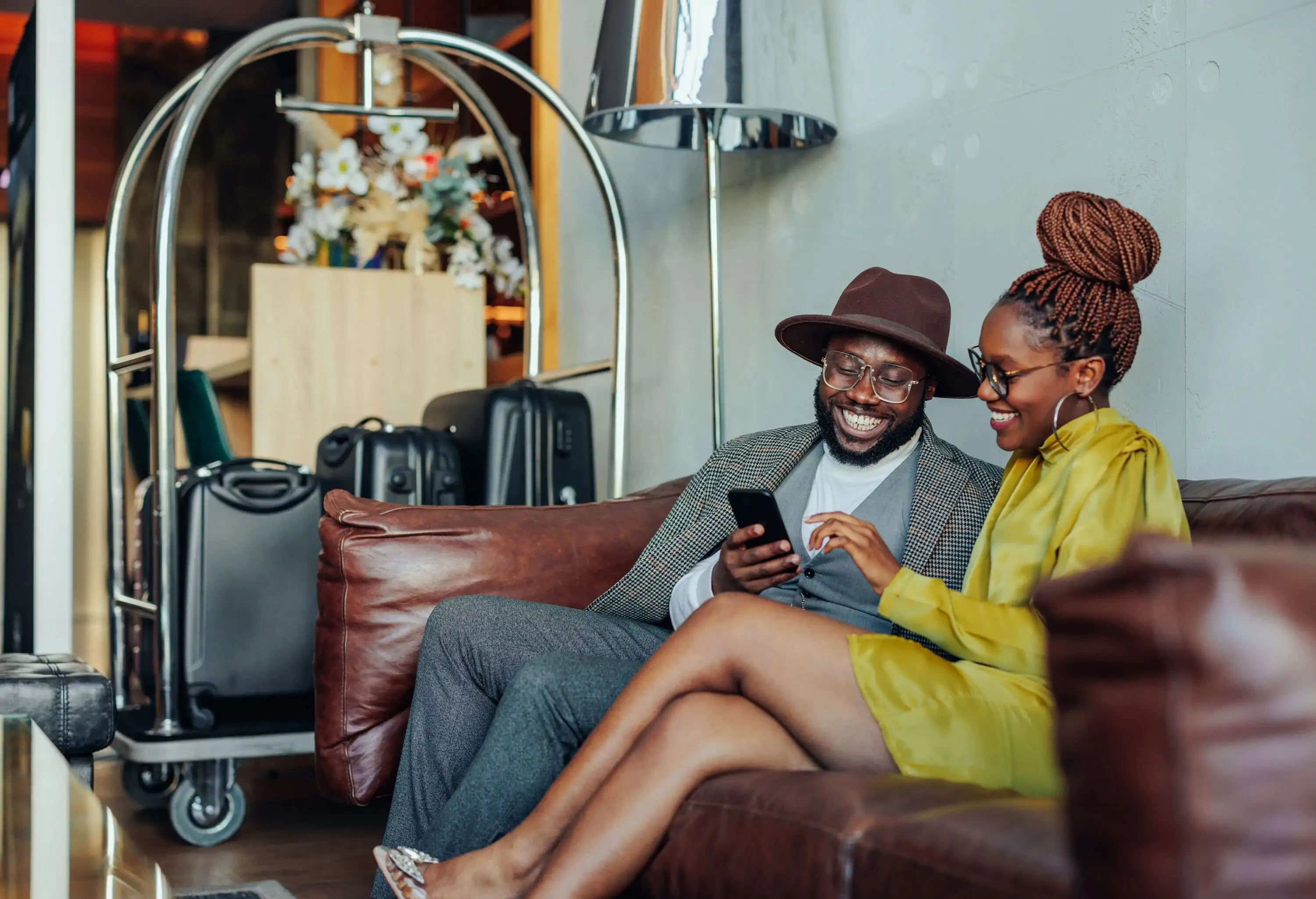 Couple sitting on a sofa with their luggage on the cart using a smartphone.