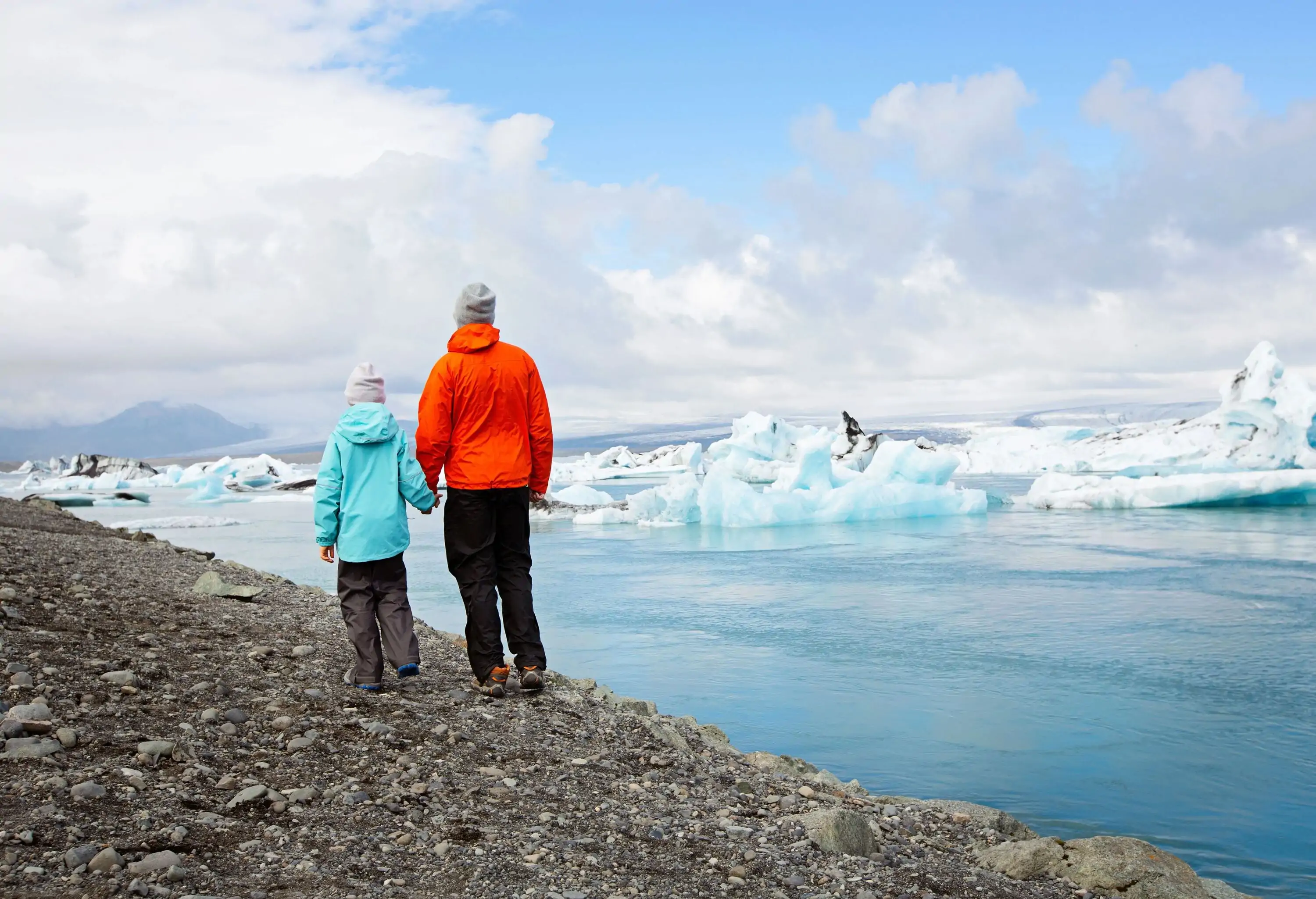 A father and son watching the icebergs drift in the water from the coast.