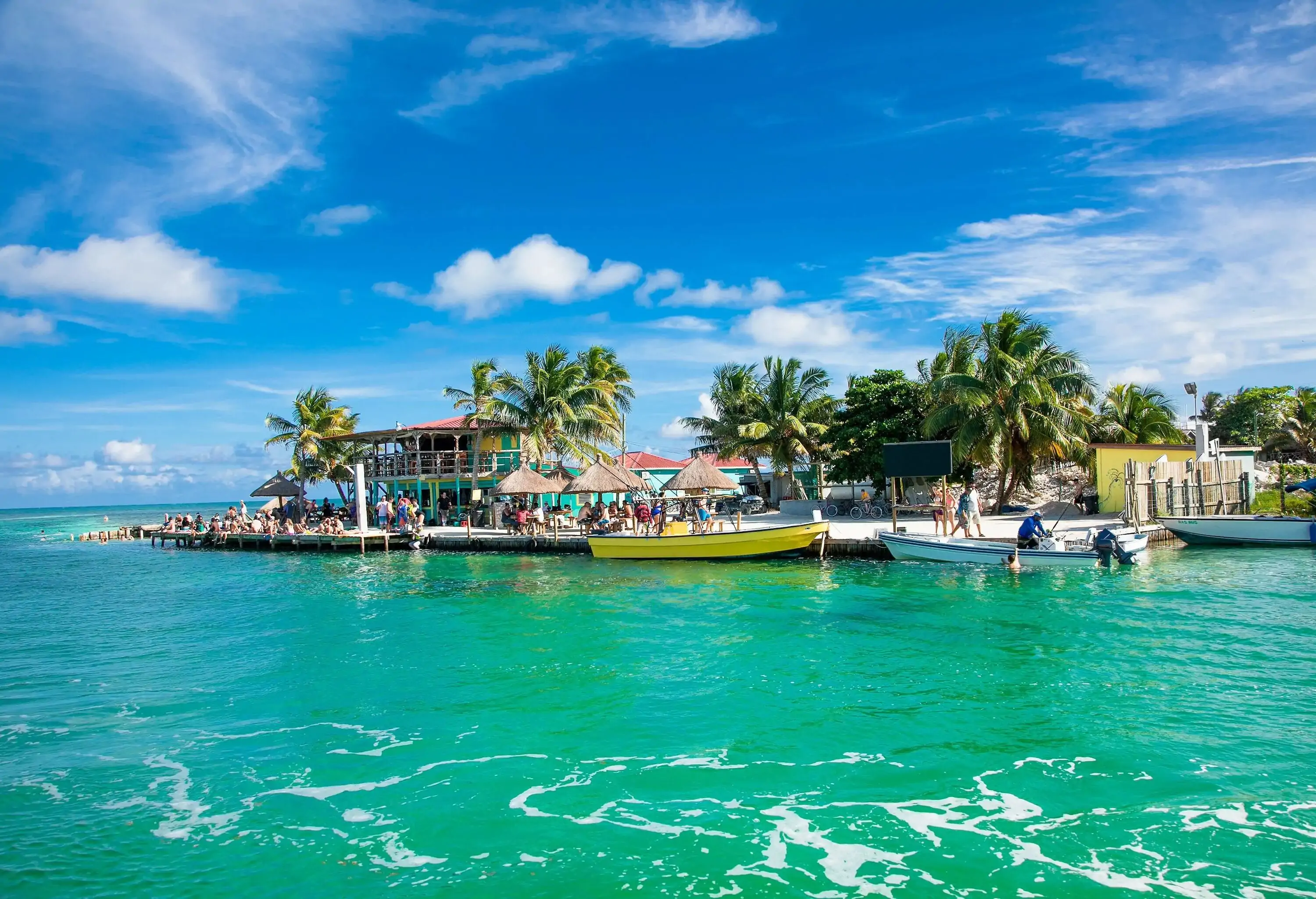 Boats moored in the jetty by the turquoise sea against the cloudy blue sky.