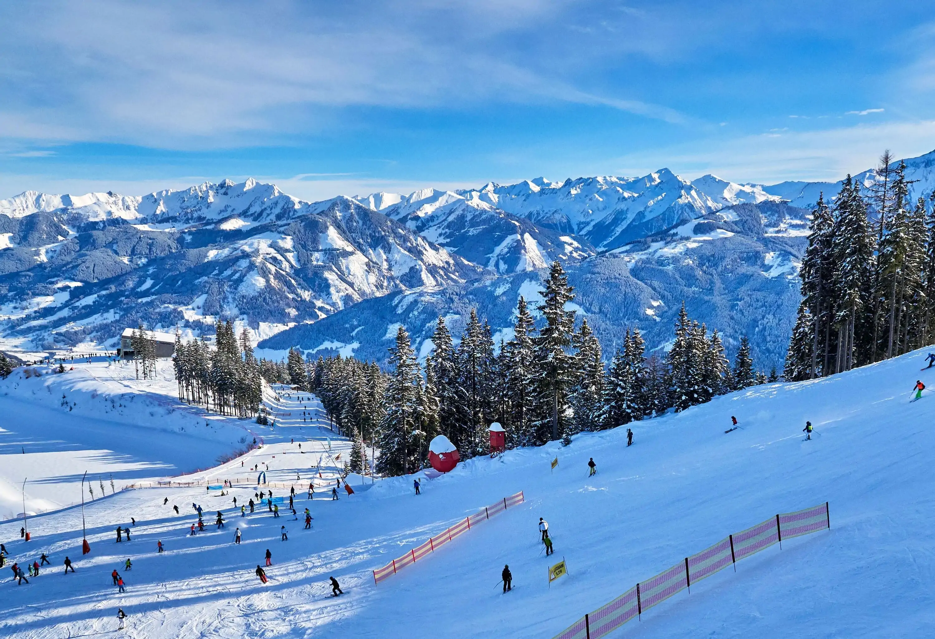 A ski resort with people enjoying winter activities and a beautiful snow-covered mountain range in the background.