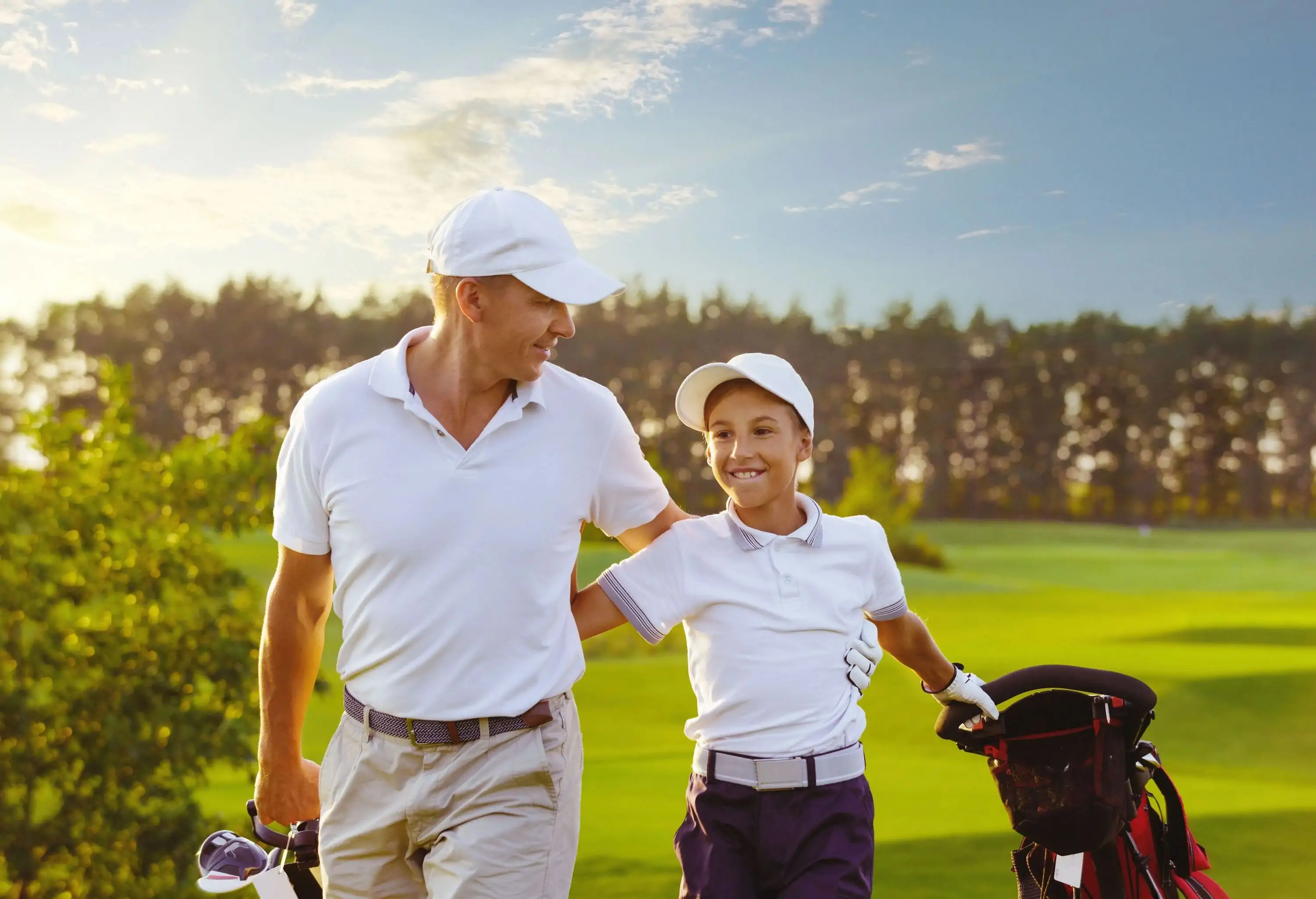 A happy father and son in a matching white shirt walking on a verdant golfing course.