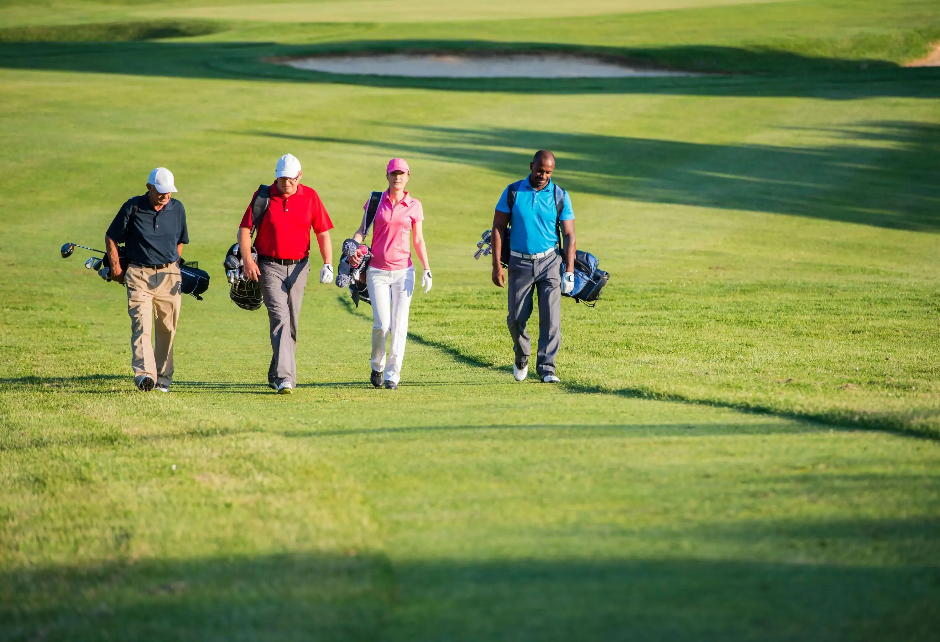 Four golfers with their gold equipment walk on a lush golf course.