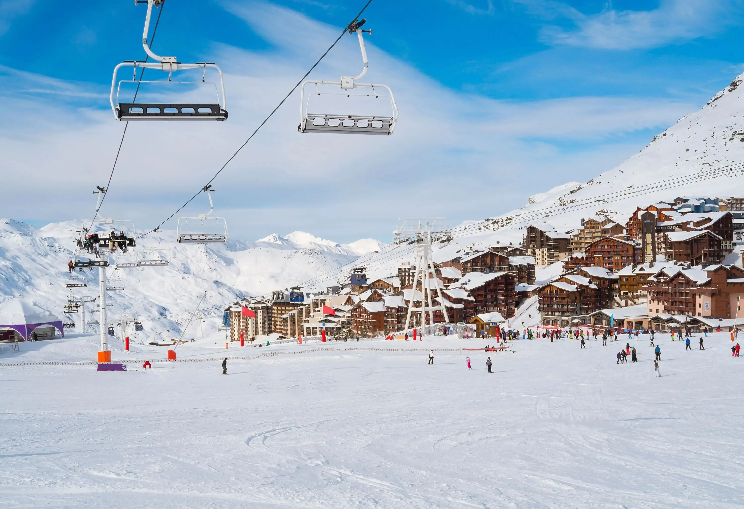 A bustling ski resort with people moving around the snow and riding chairlifts.