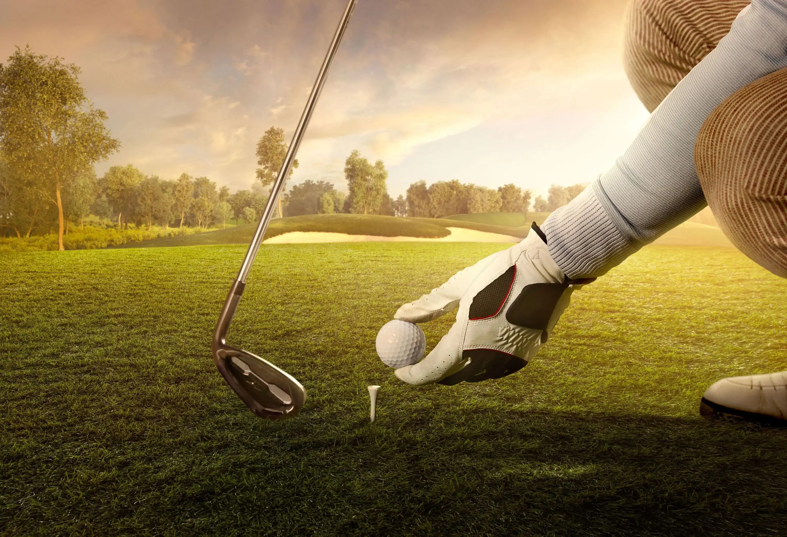 A golfer holding a club and positioning the ball on a tee.