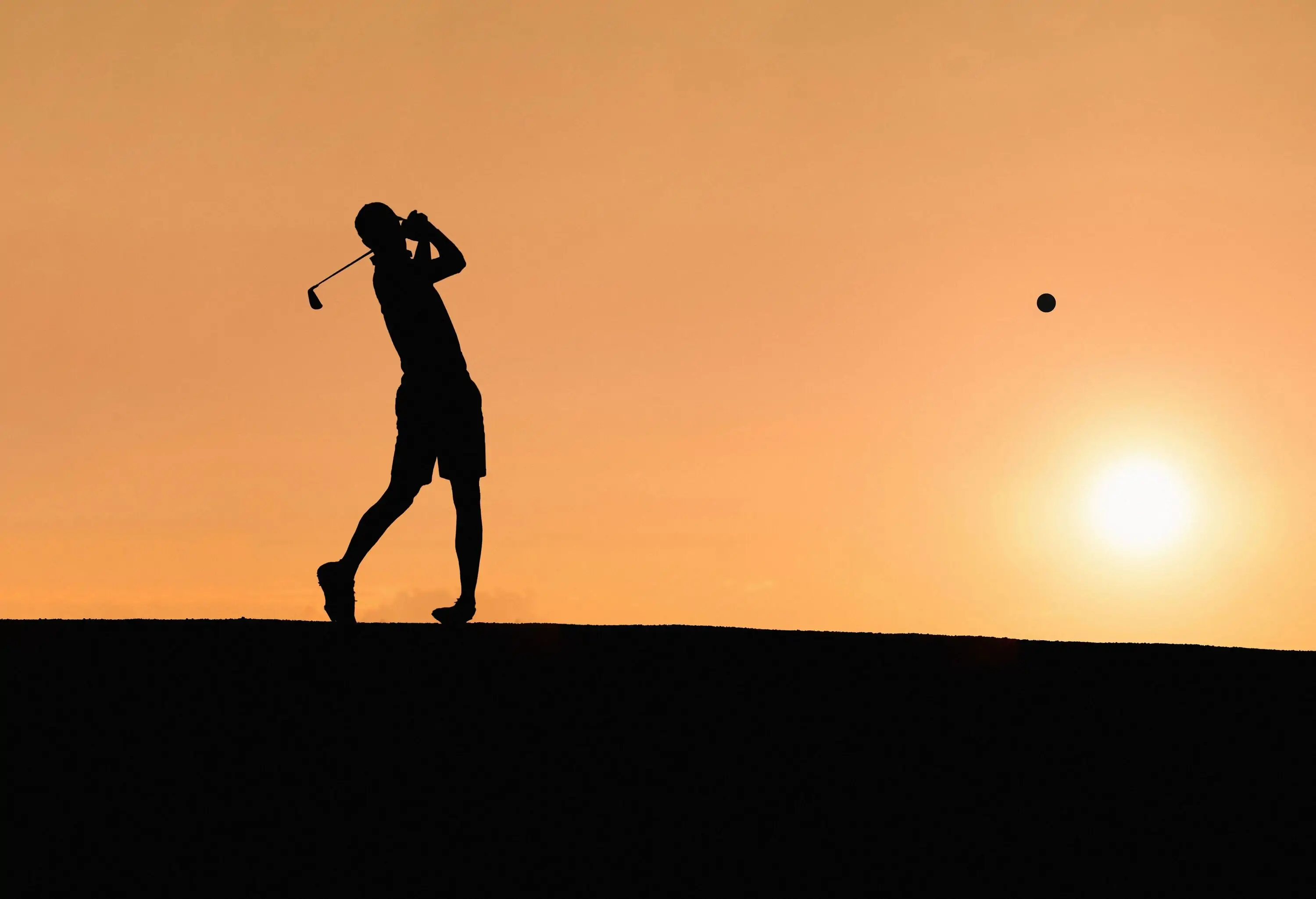 A golfer, silhouetted against the sky, executes the perfect pitch with grace and poise.