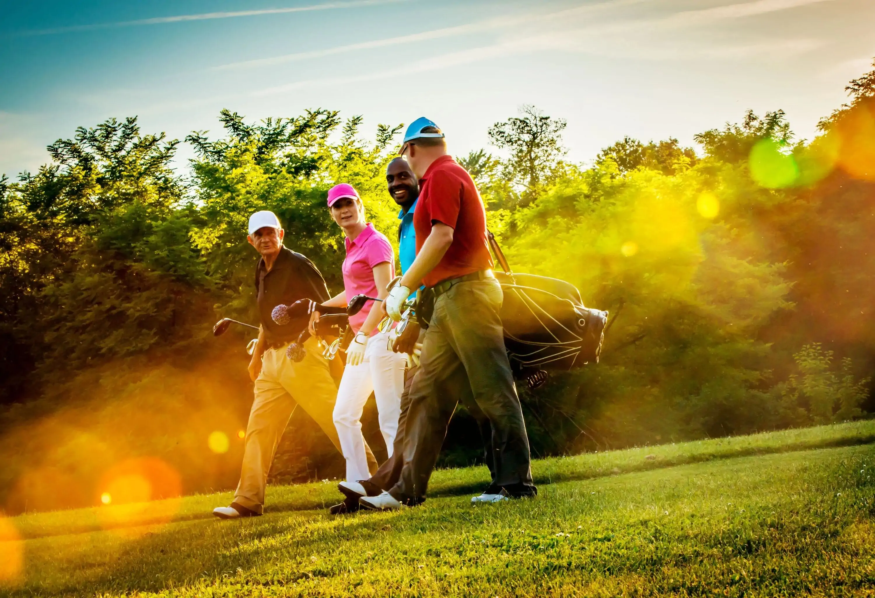 Four male friends wearing different vibrant shirts carrying their equipment while walking on the golf course.