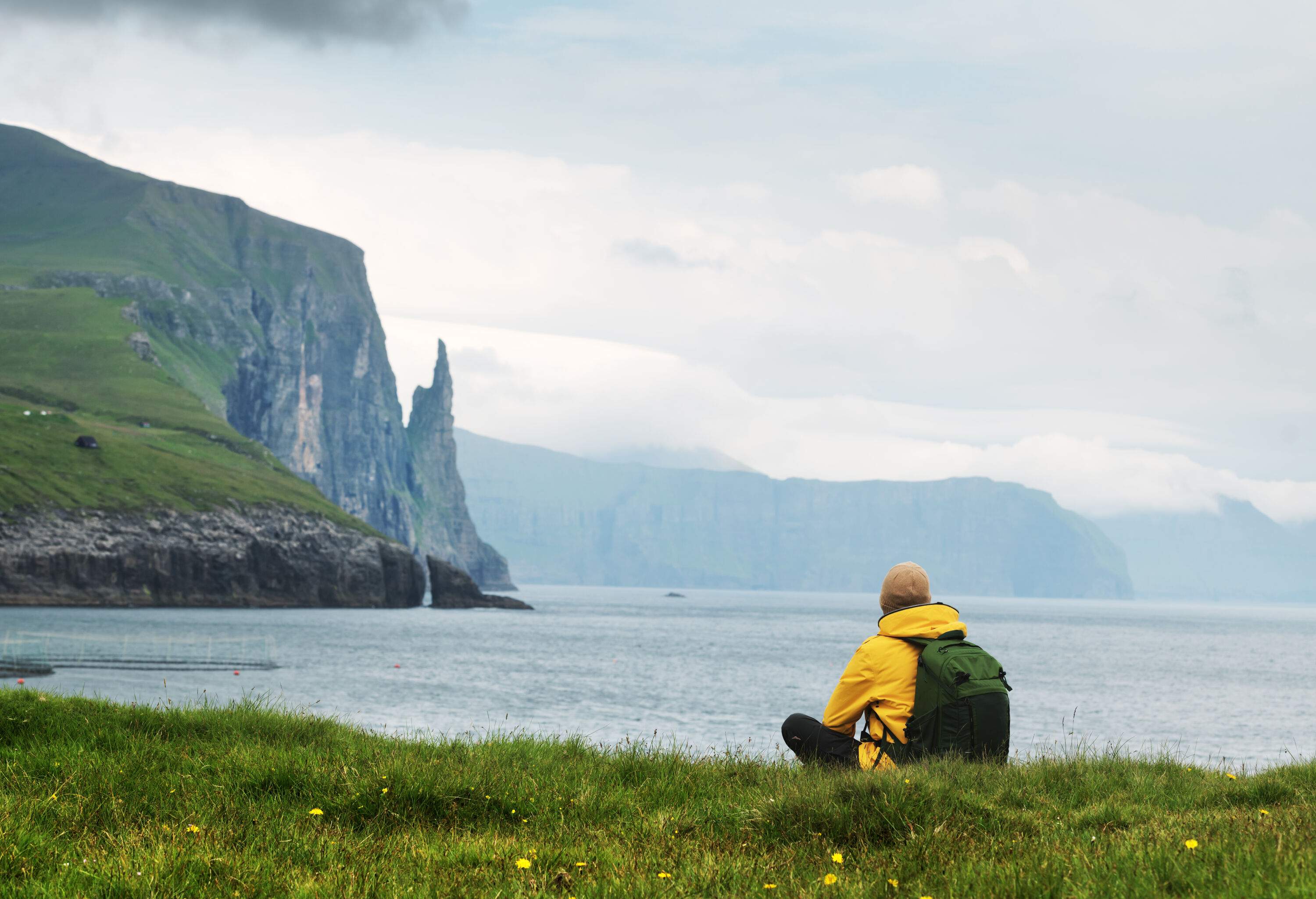 A man sitting in the meadow and looking at the view of the sea and the Witches Finger cliffs rising from the water.