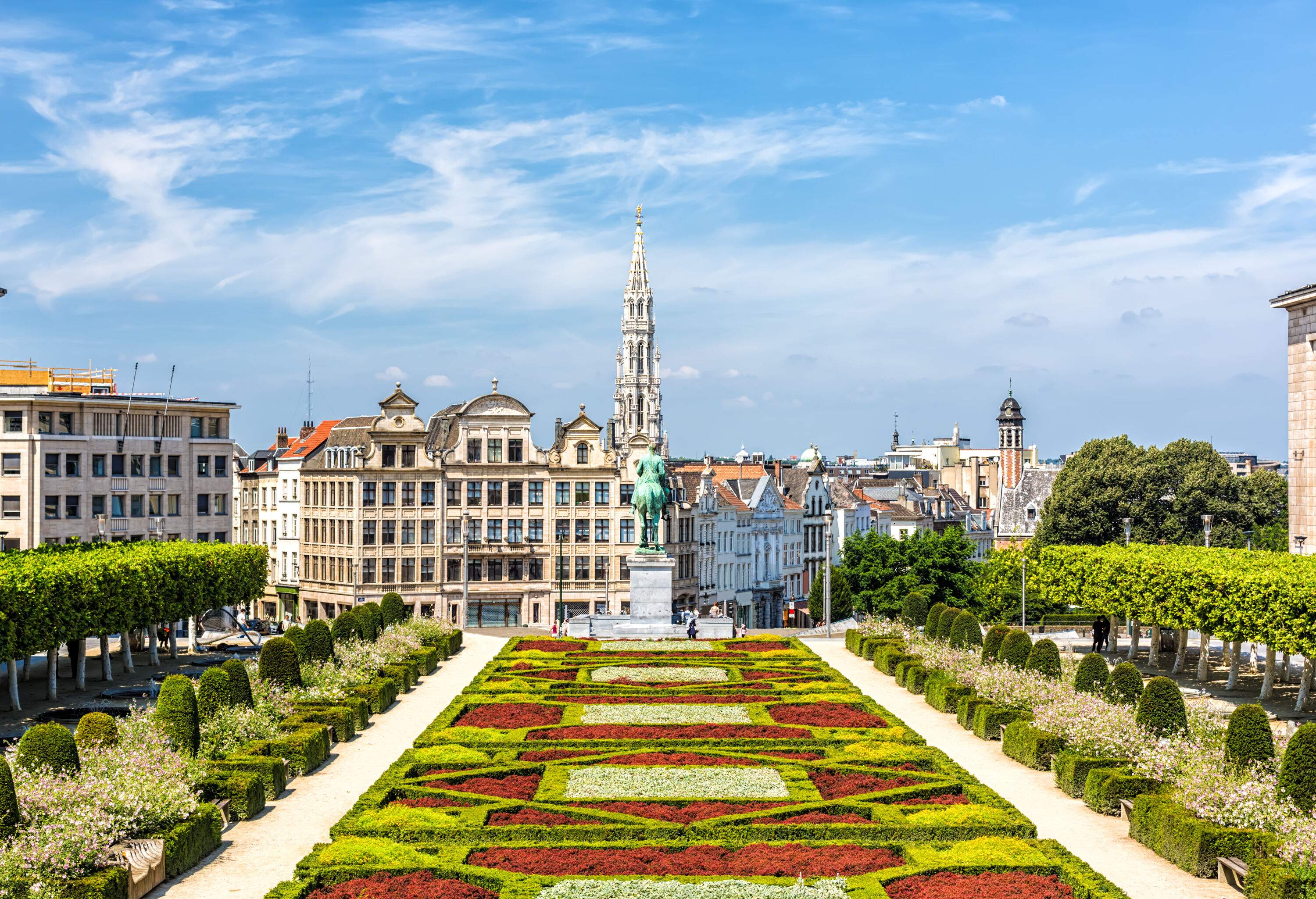 A public garden with a scenic landscape with a statue facing the cluster of medieval buildings protruding to the dramatic sky.