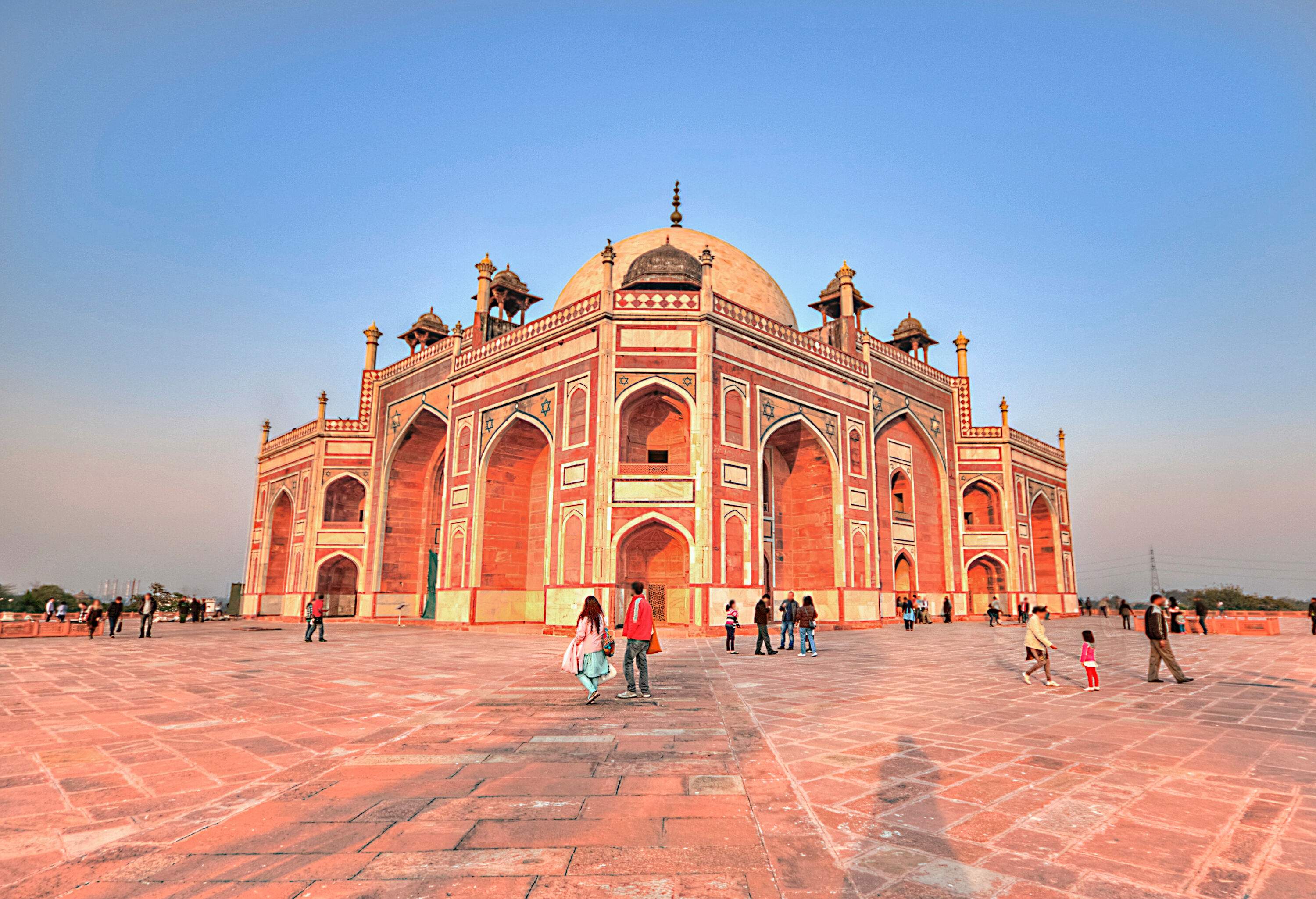 People wandering across the square in front of Humayun’s Tomb, which is set against a clear sky.