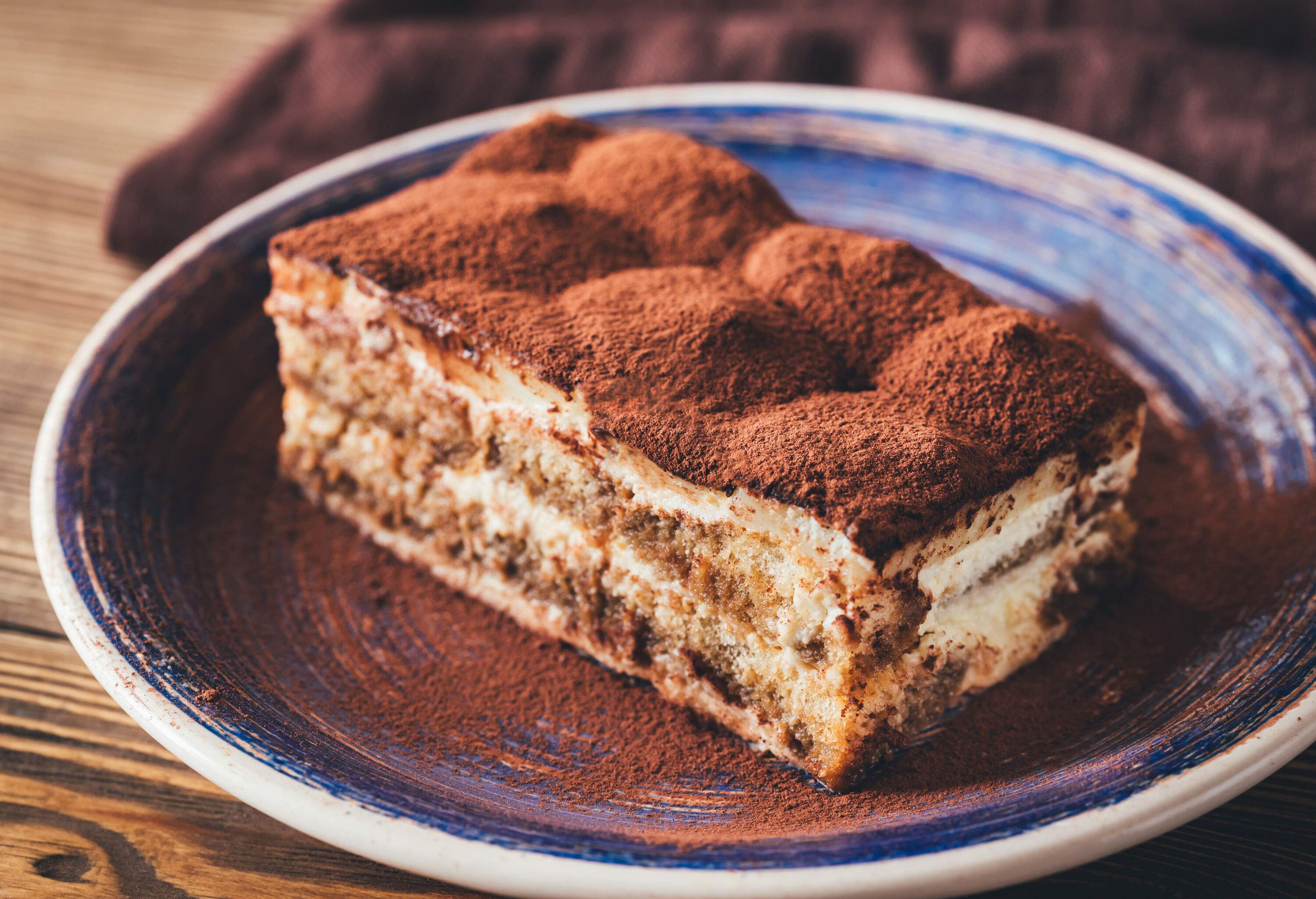 A slice of a tiramisu dessert served on a small blue, curved plate.