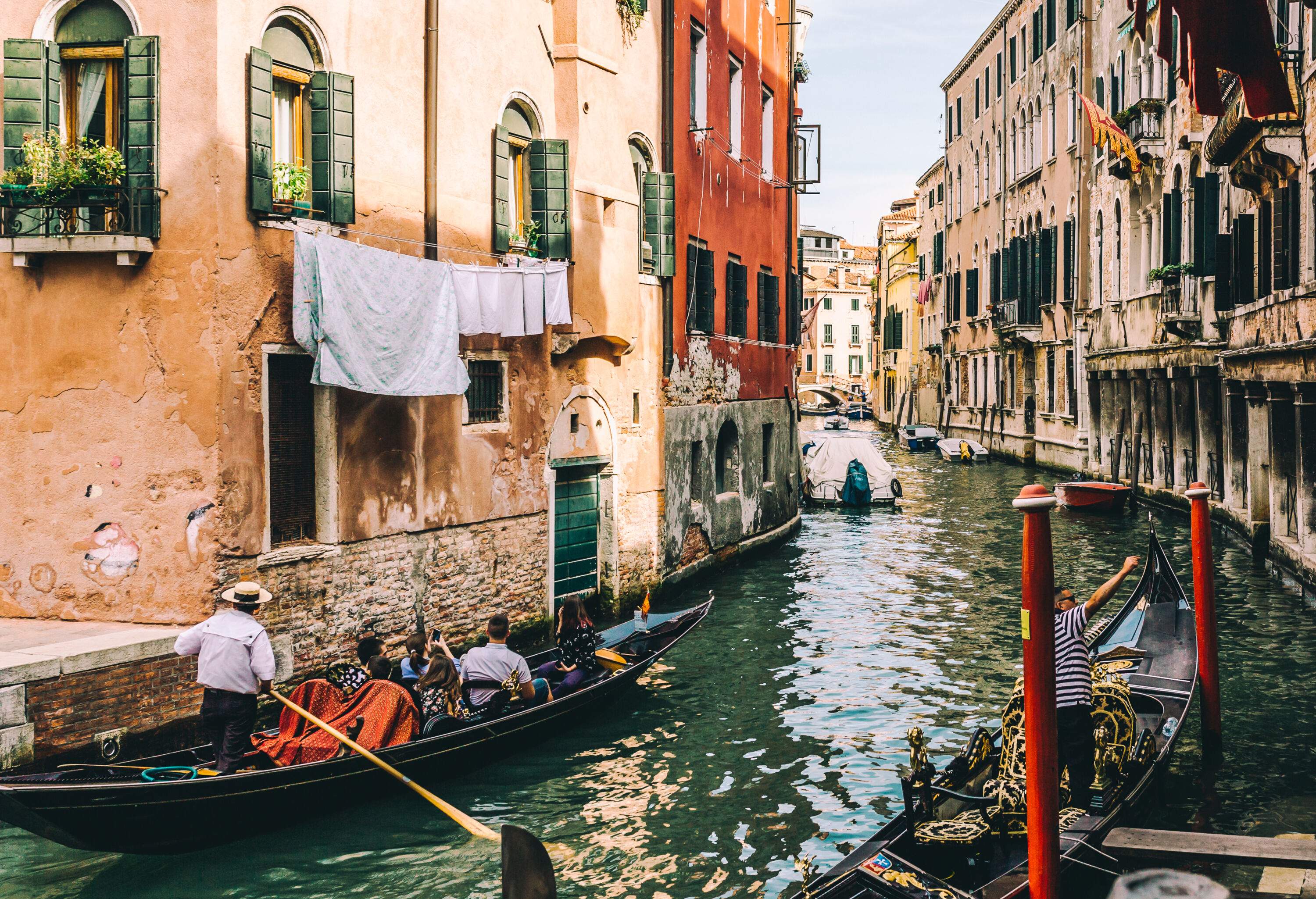 Gondolas cruising through a canal surrounded by old buildings on both banks.