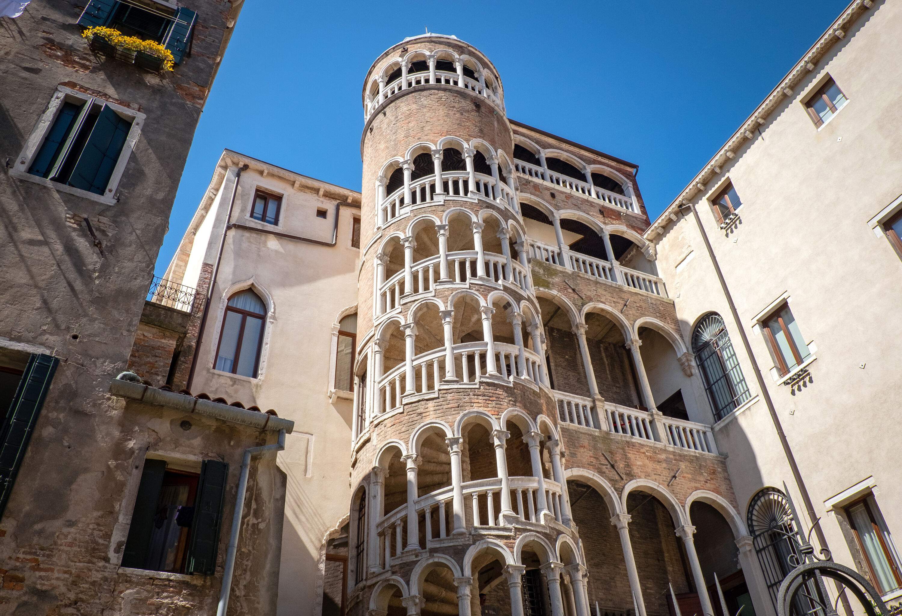 A small stone building with a spiral staircase and multistorey arcades against a blue sky.