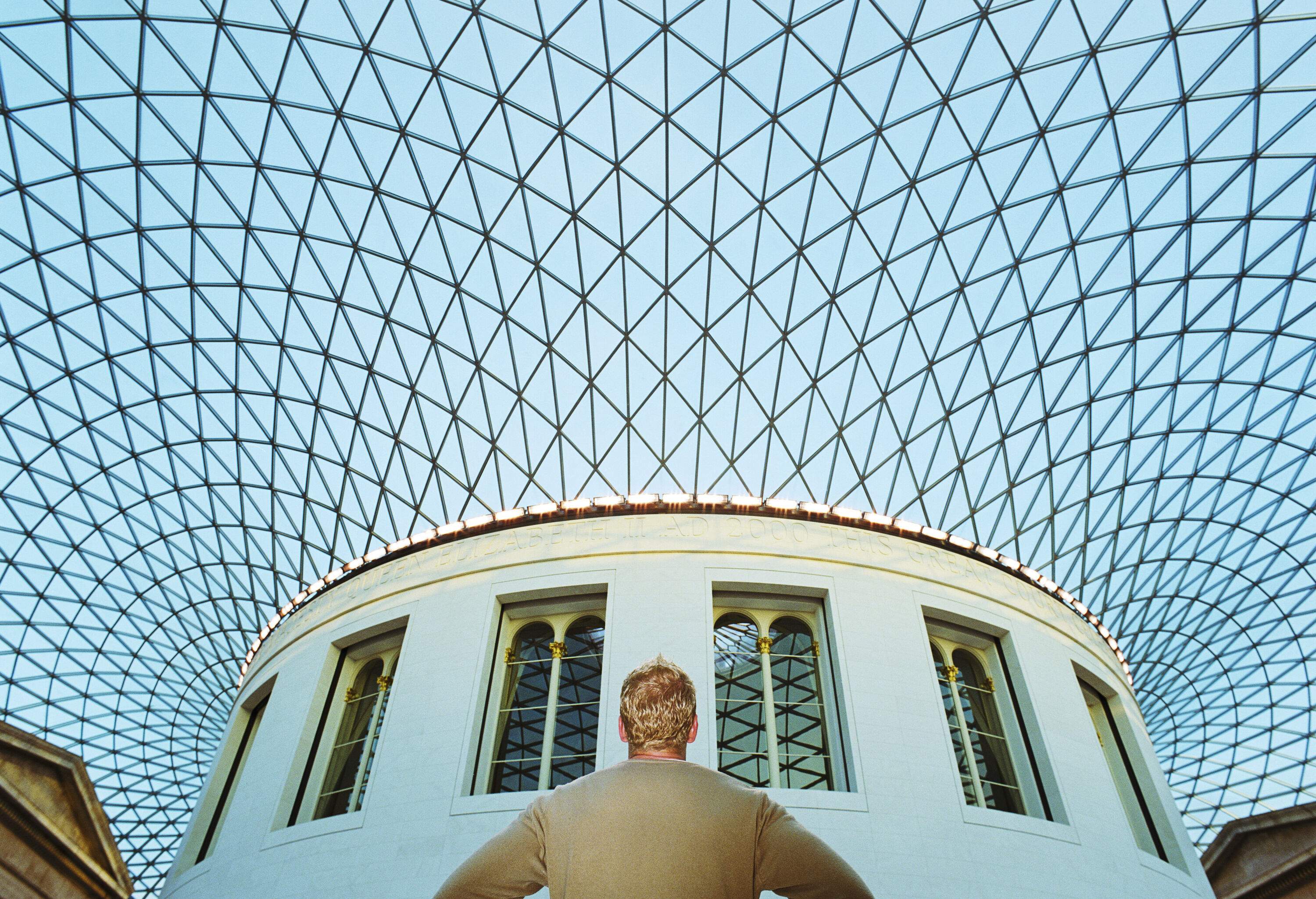 A man inside the covered courtyard looks above the glass panes ceiling that forms a spectacular, light-filled atrium.