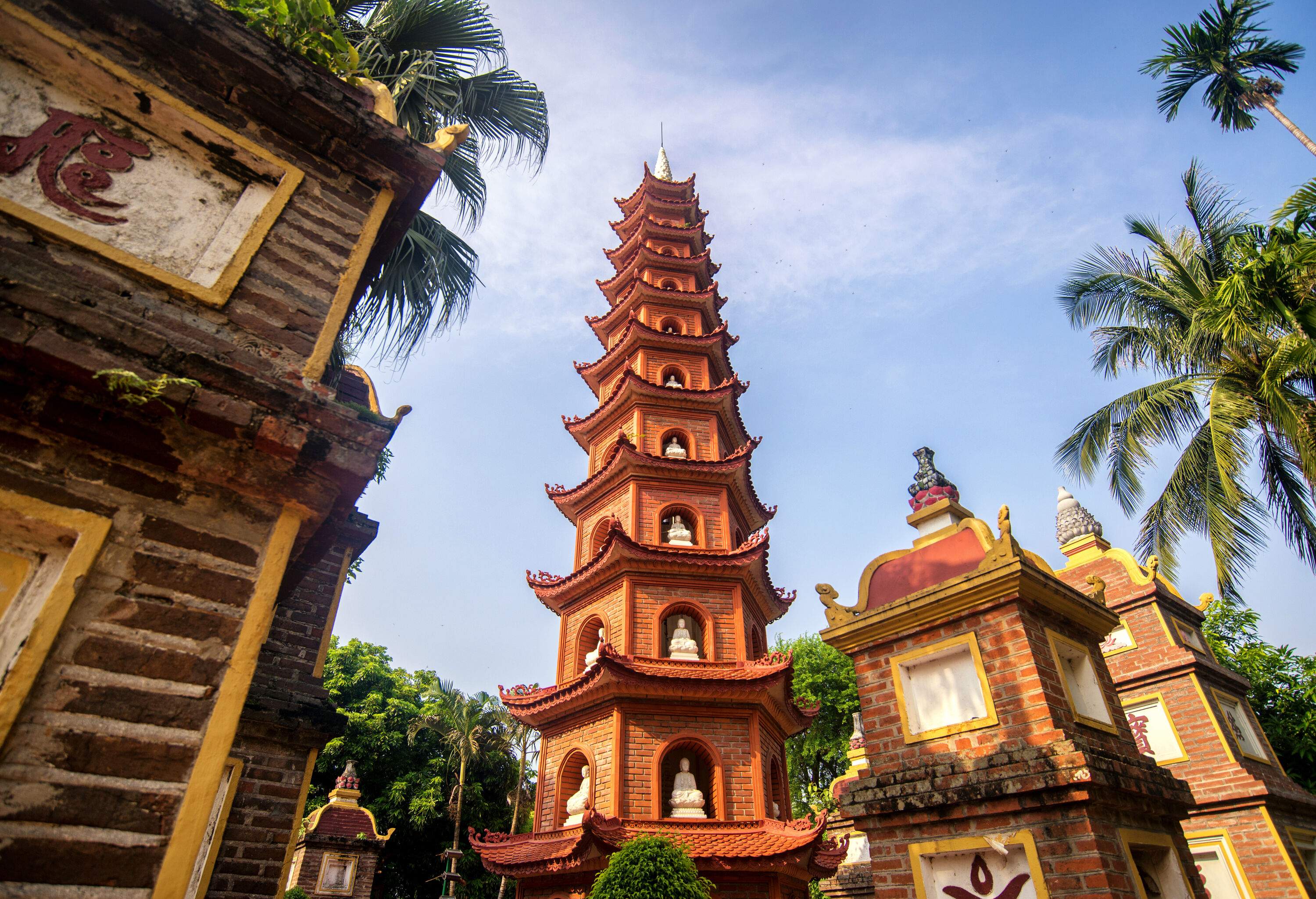 A tiered pagoda made of red bricks in a park with palm trees.