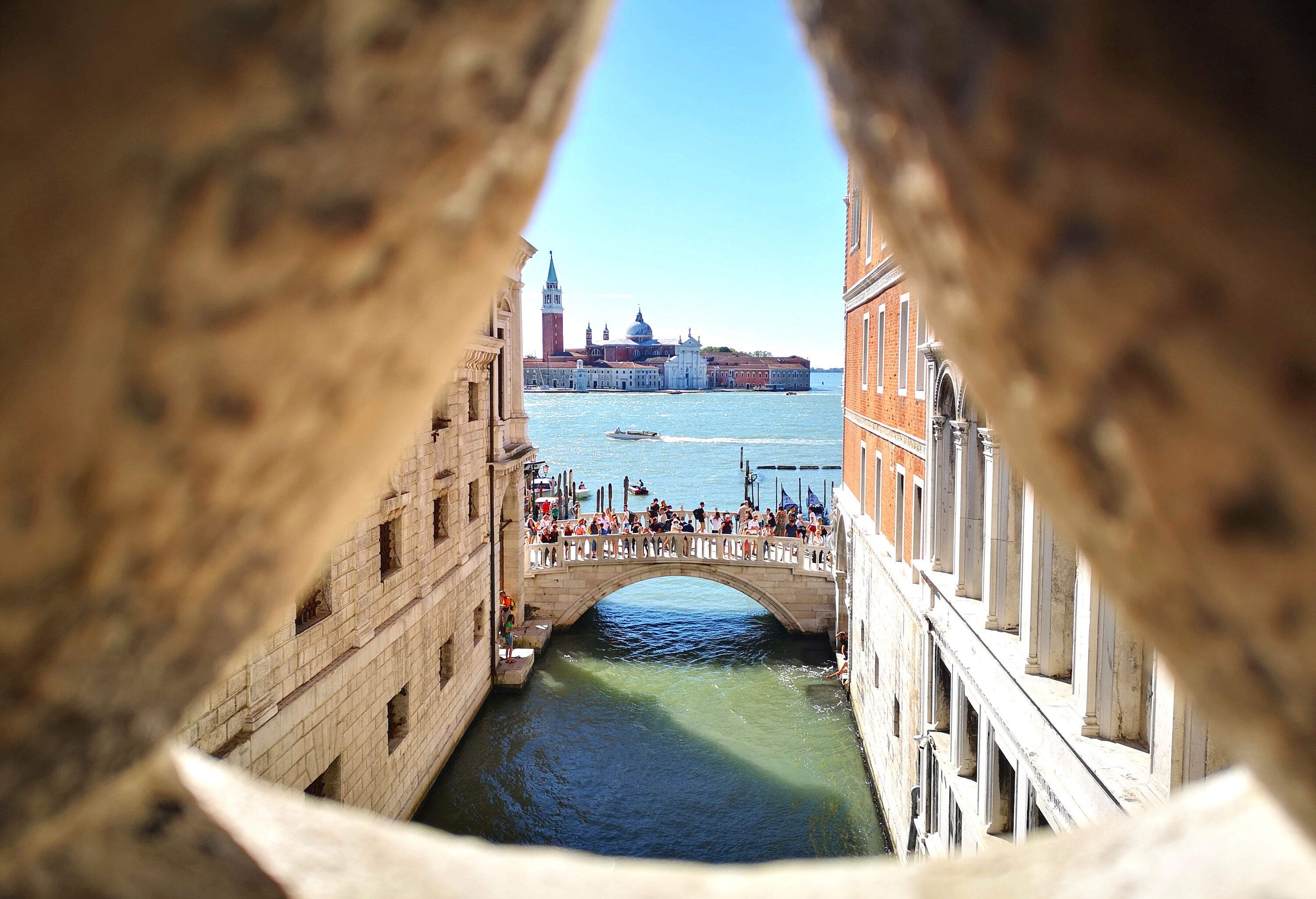 A crowd on a historic arched bridge over the sea is seen from a building window.