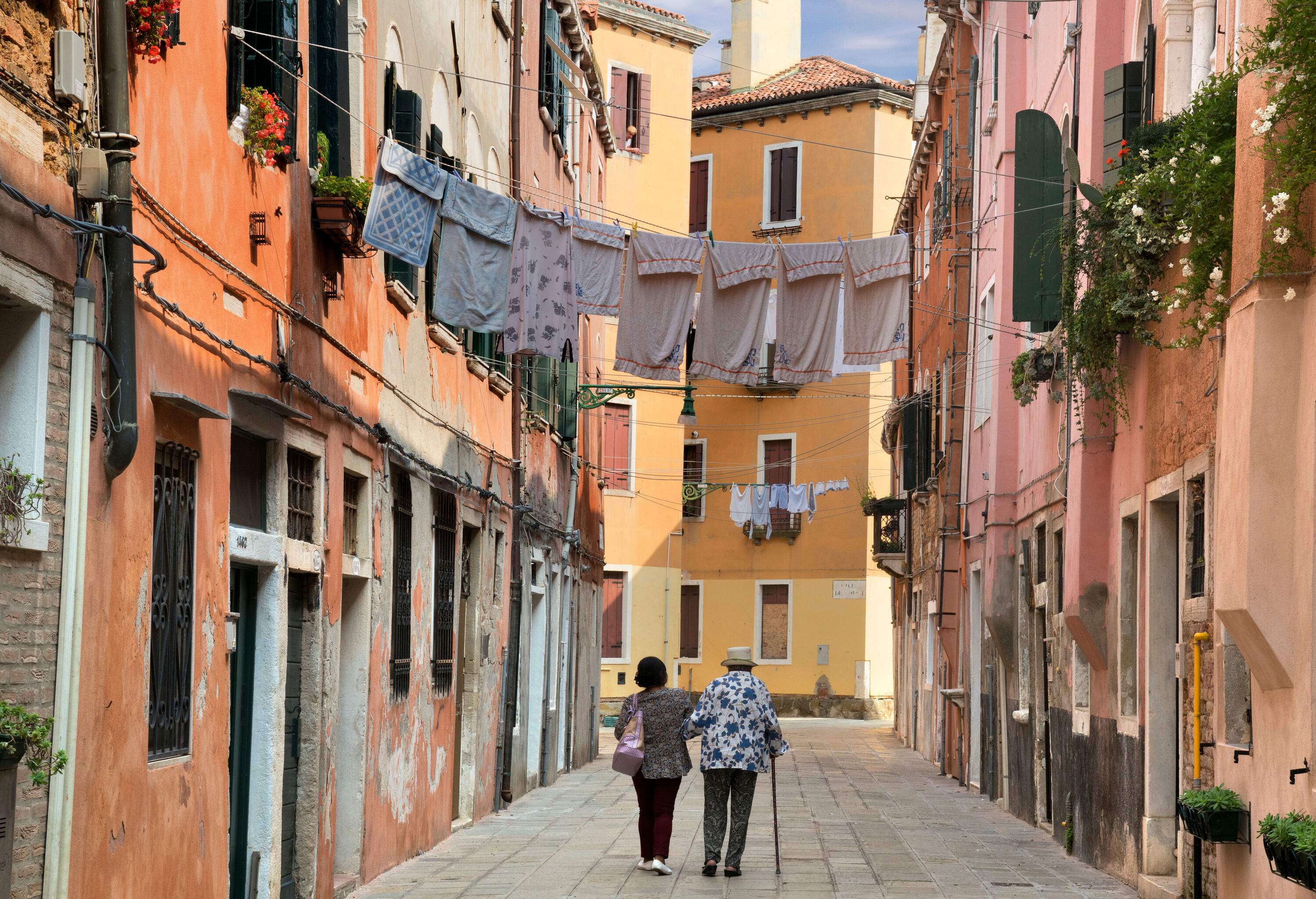 A lady ambles with a senior in a narrow street between the colourful residential houses.