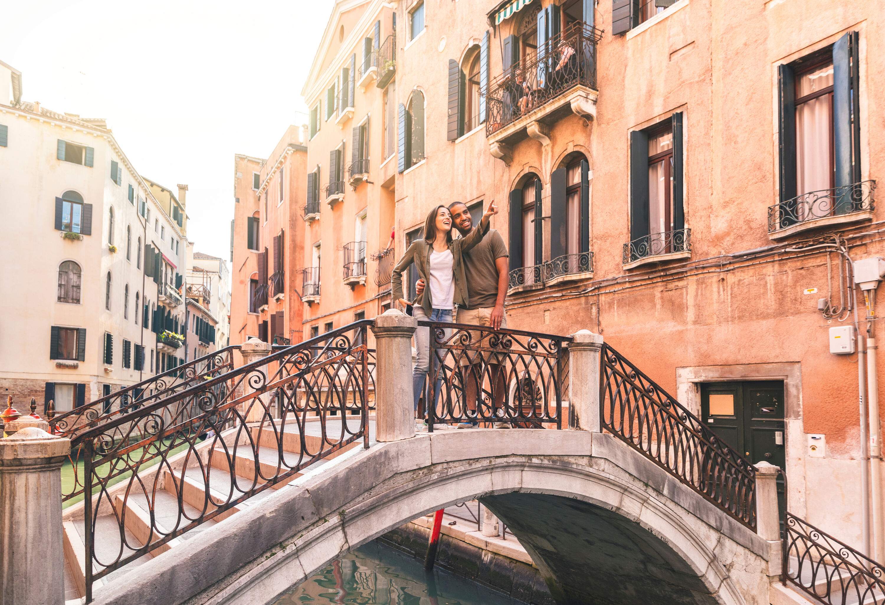 A woman points at something as she stands beside a man on an arch bridge.