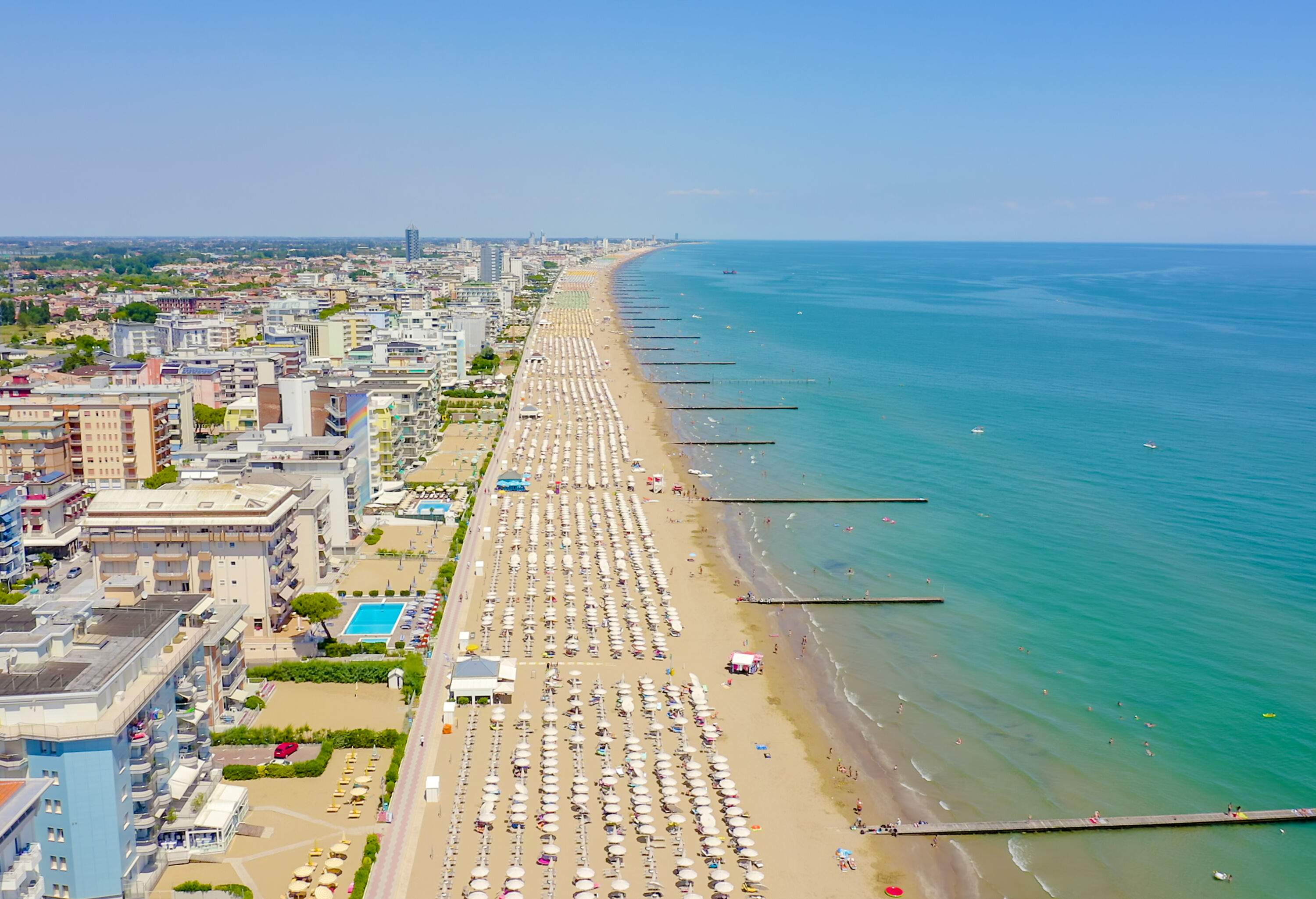 A long stretch of a white sand beach lined with numerous white umbrellas in rows along compact buildings.