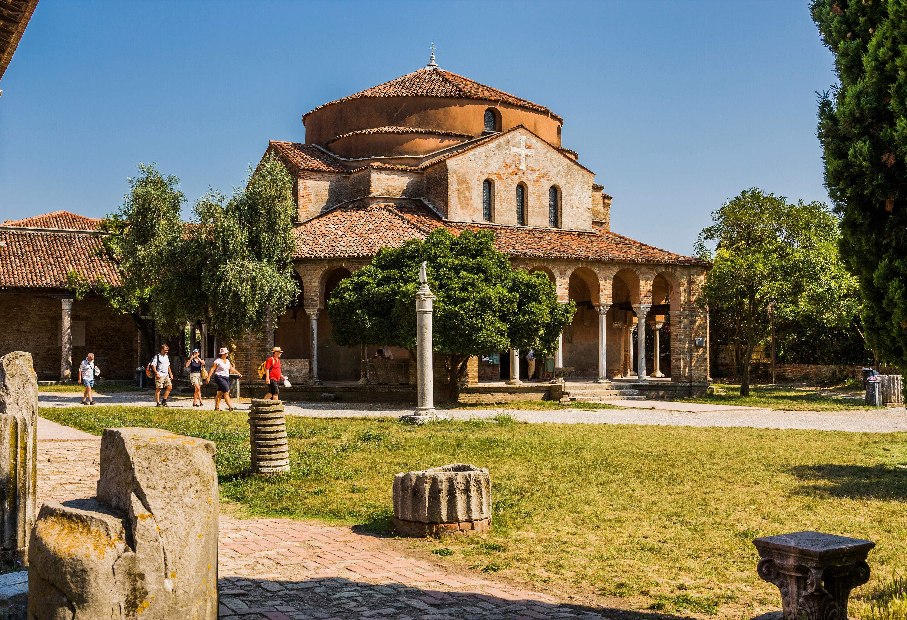 A group of people strolling down a path that runs alongside a Byzantine-style church with tiled roofs.