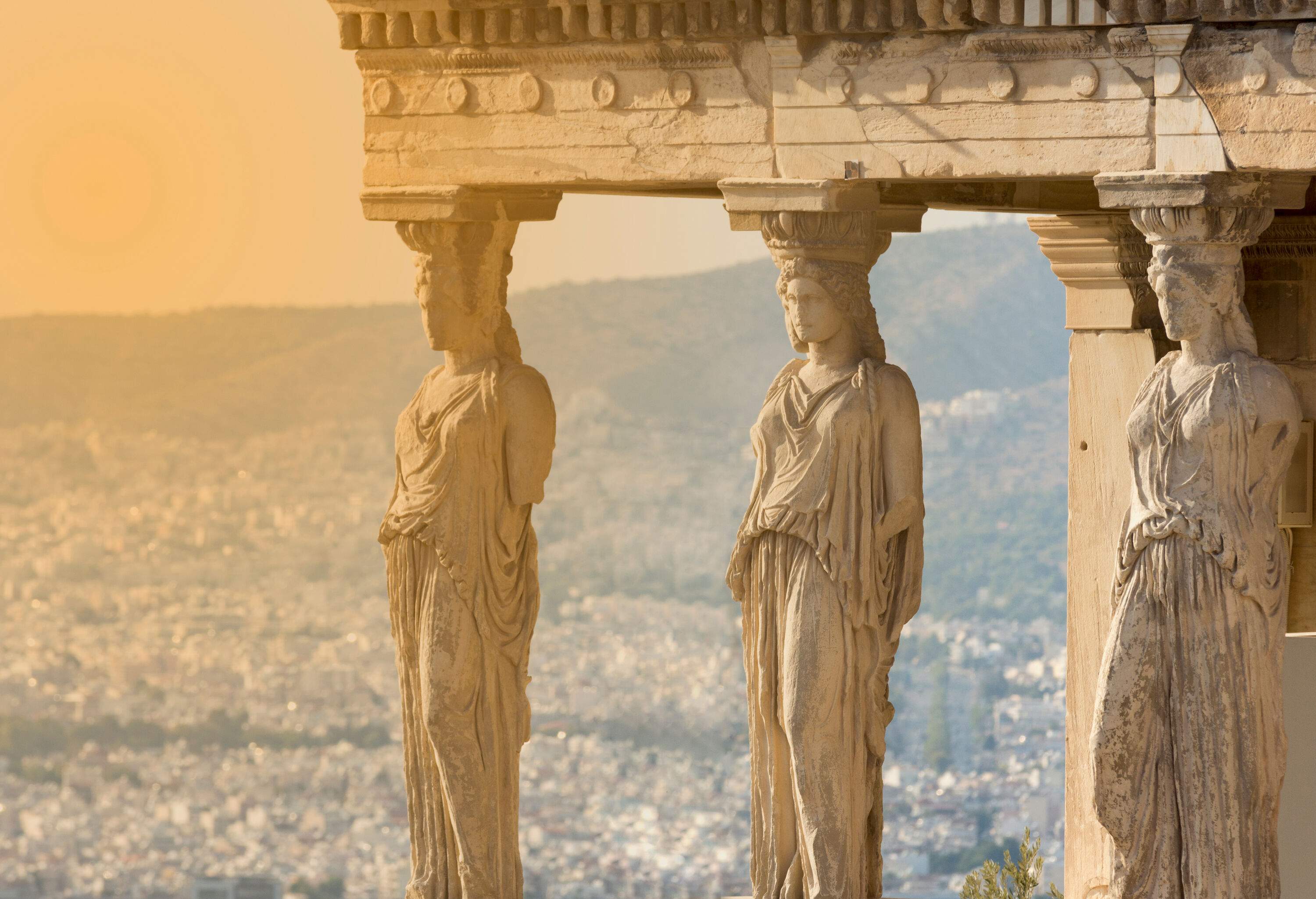 A carved female figure stands in the forecourt of the ruins of the Acropolis of Athens.