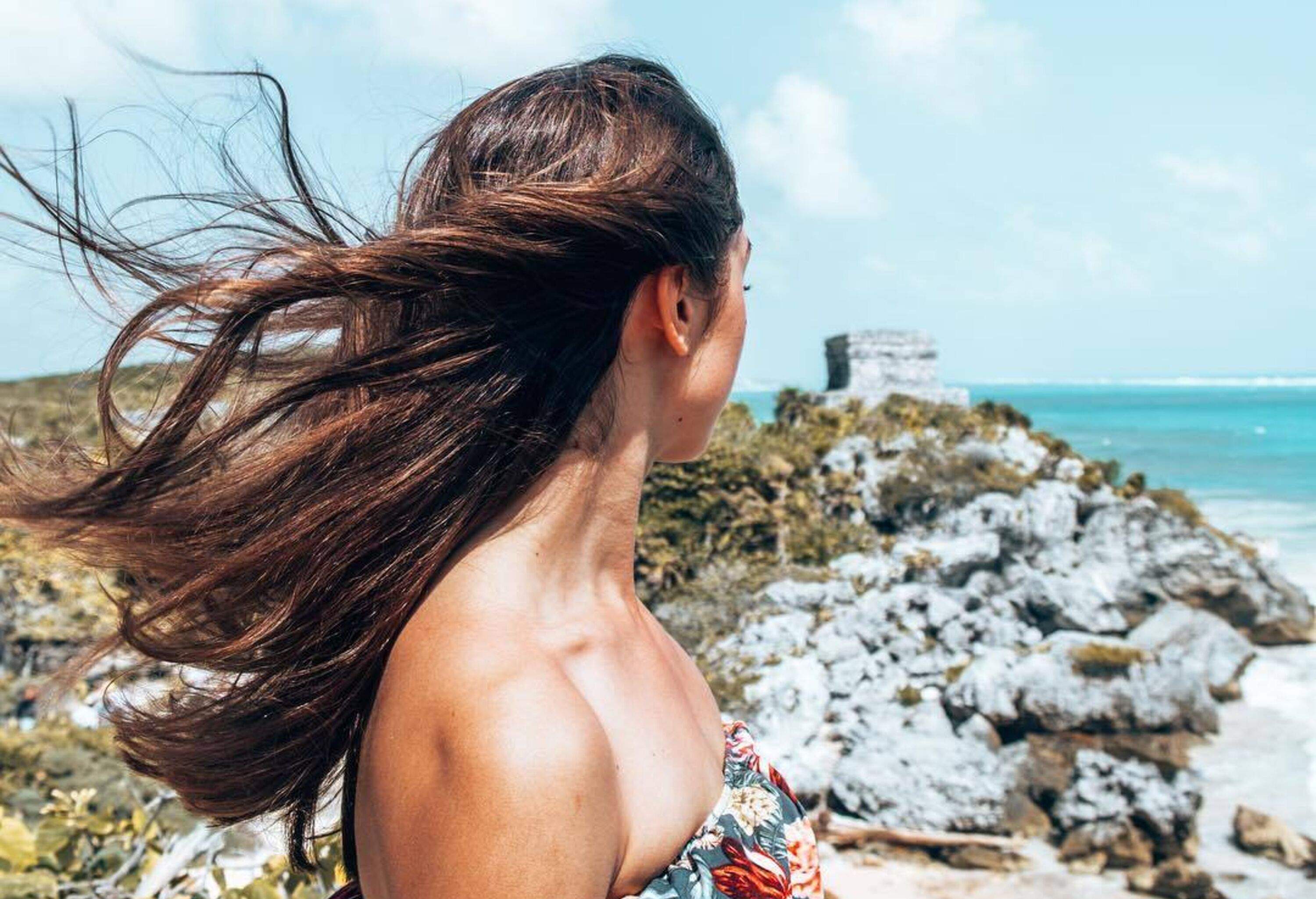 A person dressed in off-shoulder attire gazes pensively at a rugged coastal landscape.