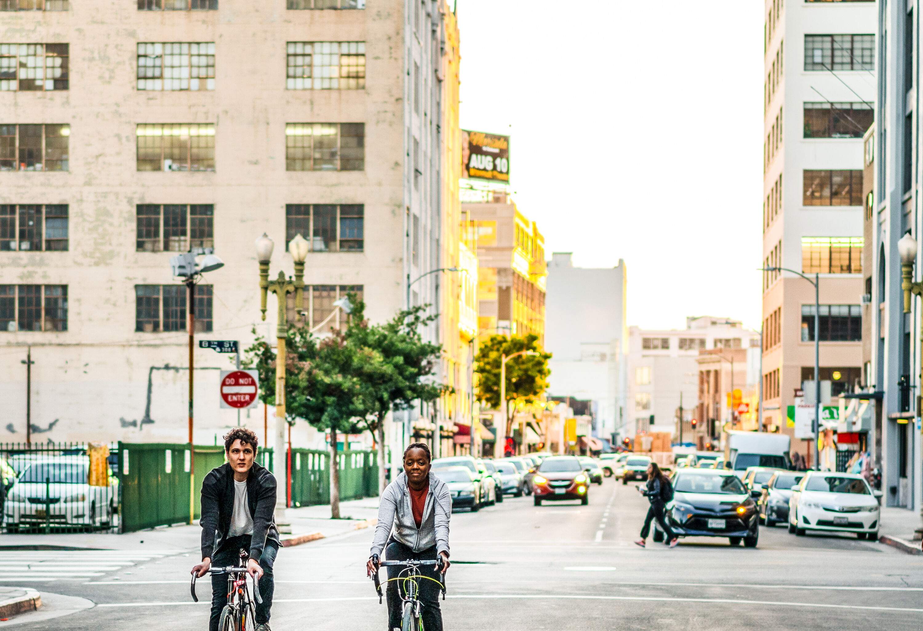 Two friends ride their bicycles down a street across tall city buildings.