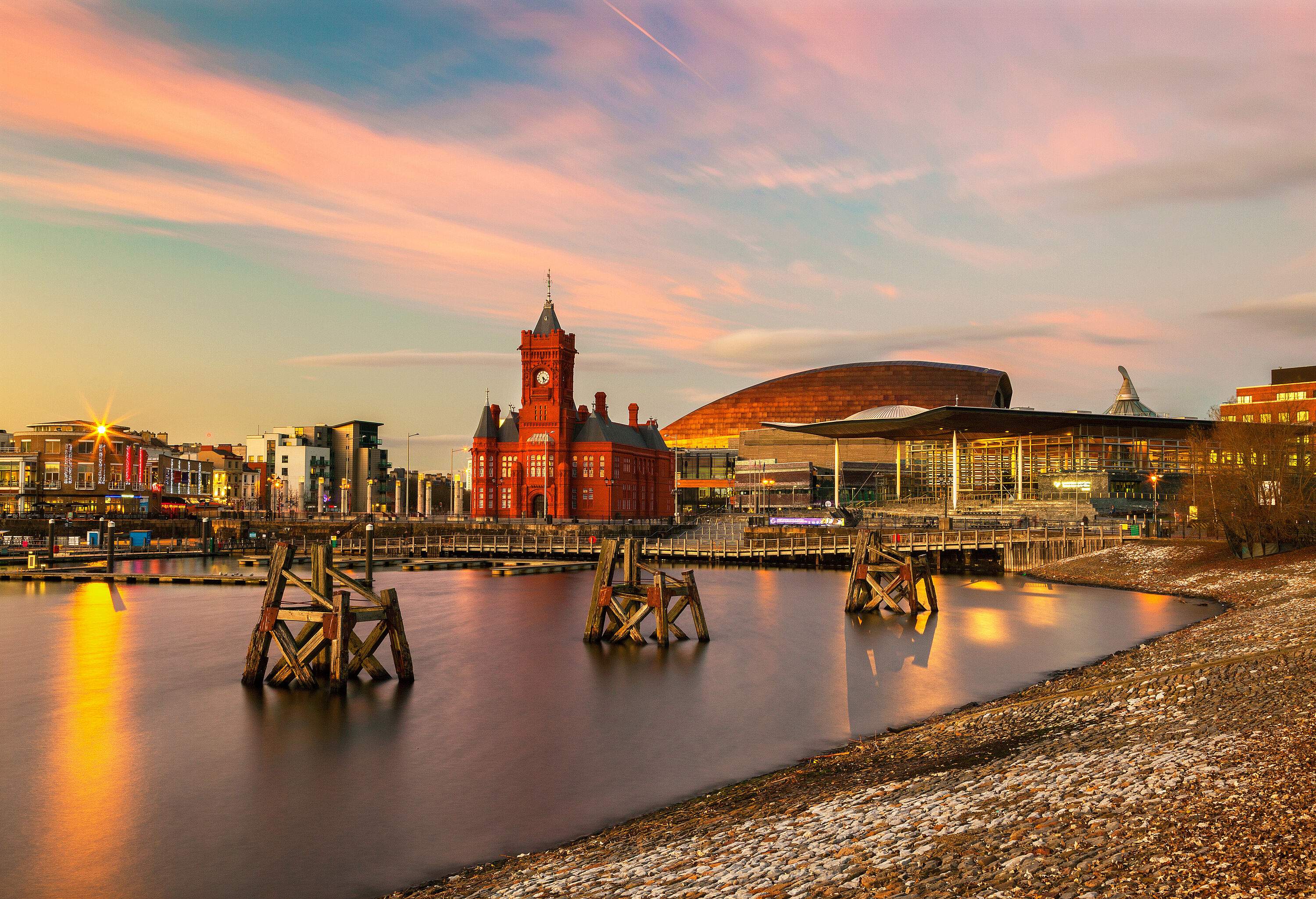 An afternoon sun shines on a city skyline along the bay, illuminating a structure with a clock tower and a copper-coloured dome structure at the back.