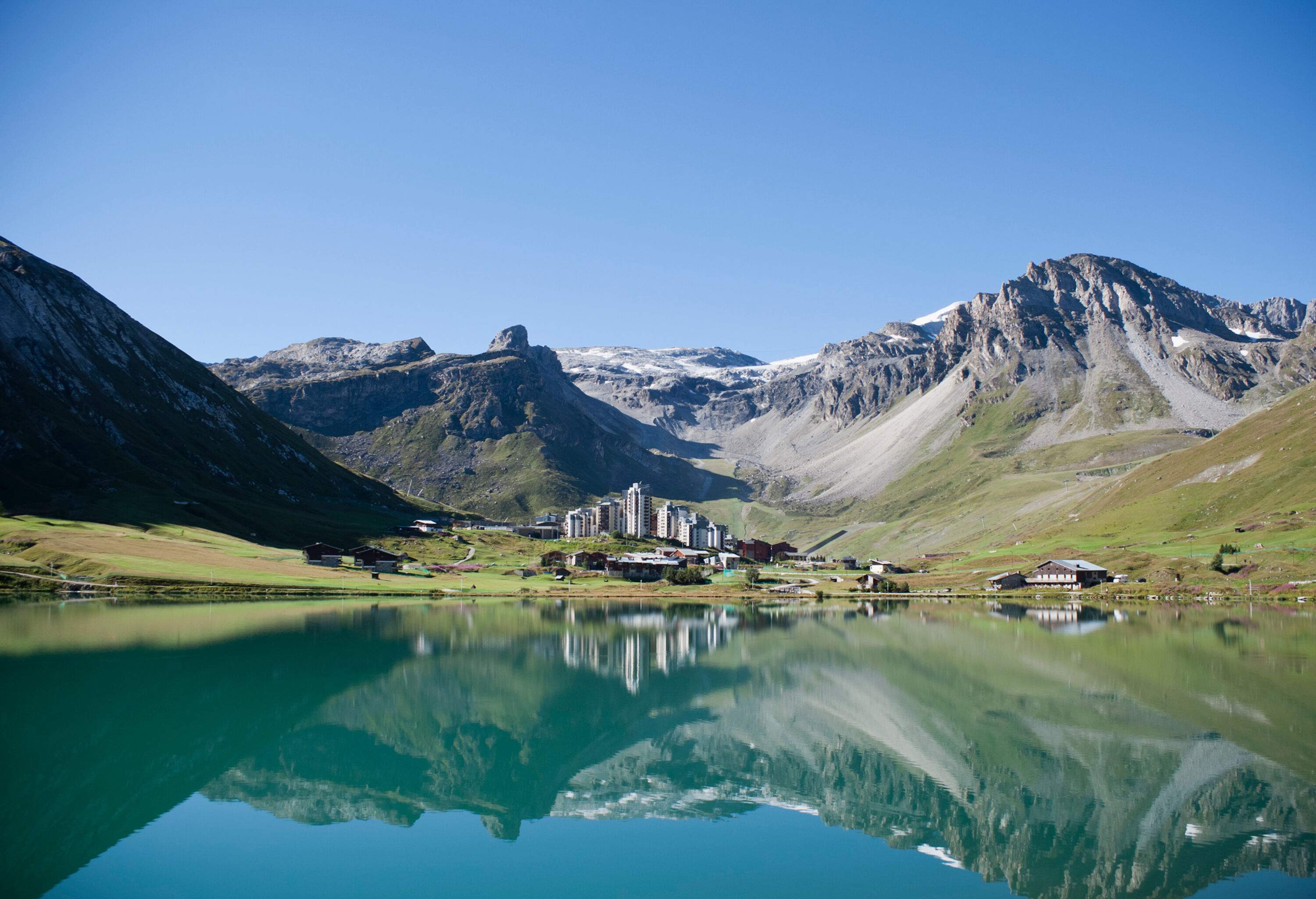 The surface of the lake reflects the tall structures of a town and the surrounding mountains.