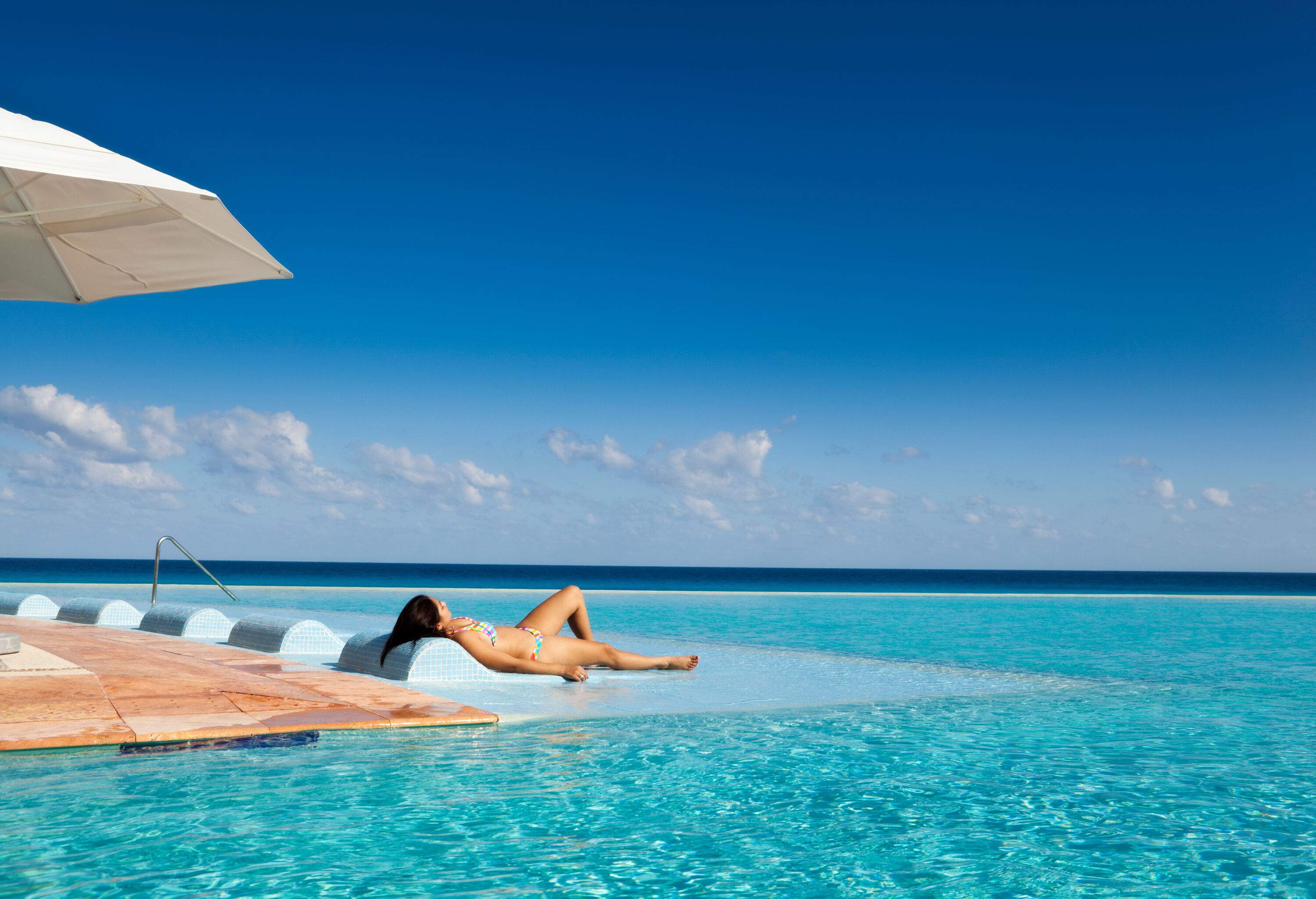 A young lady in a bikini is sunbathing on the infinity poolside overlooking the sea.