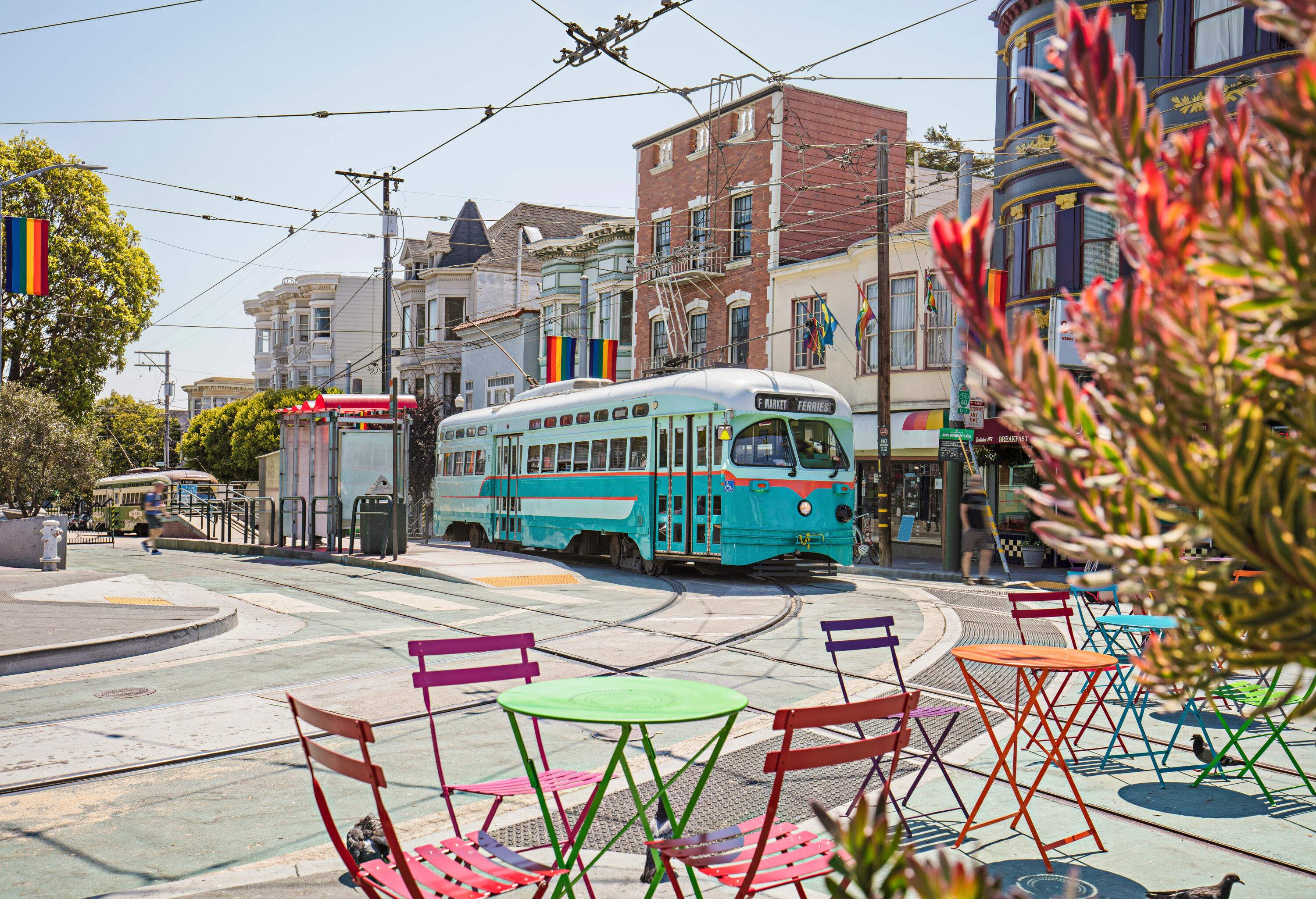 A tram travelling through Castro streets with colourful garden tables and chairs.