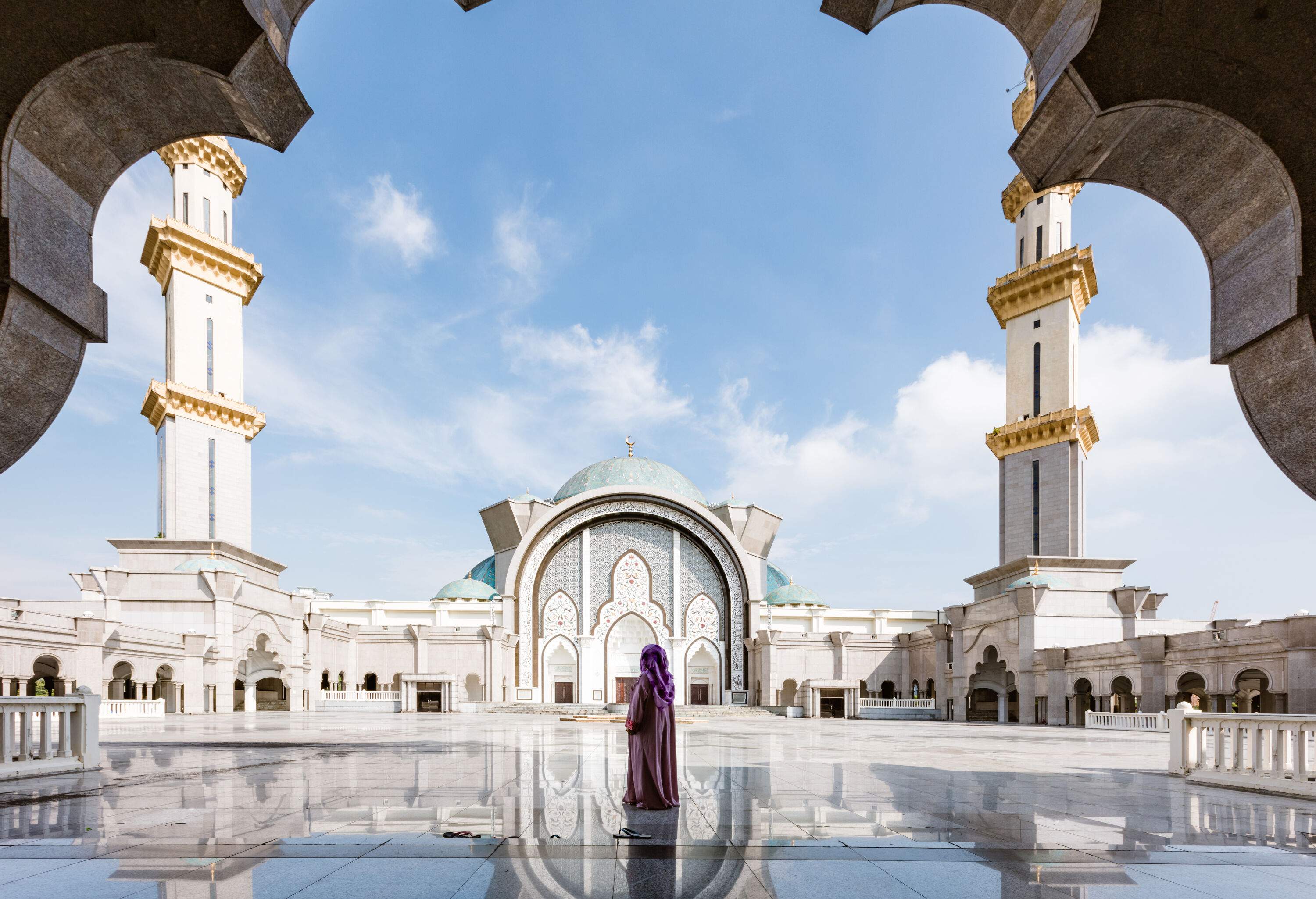 A rear view of a woman standing in the middle of a sparking mosque courtyard.