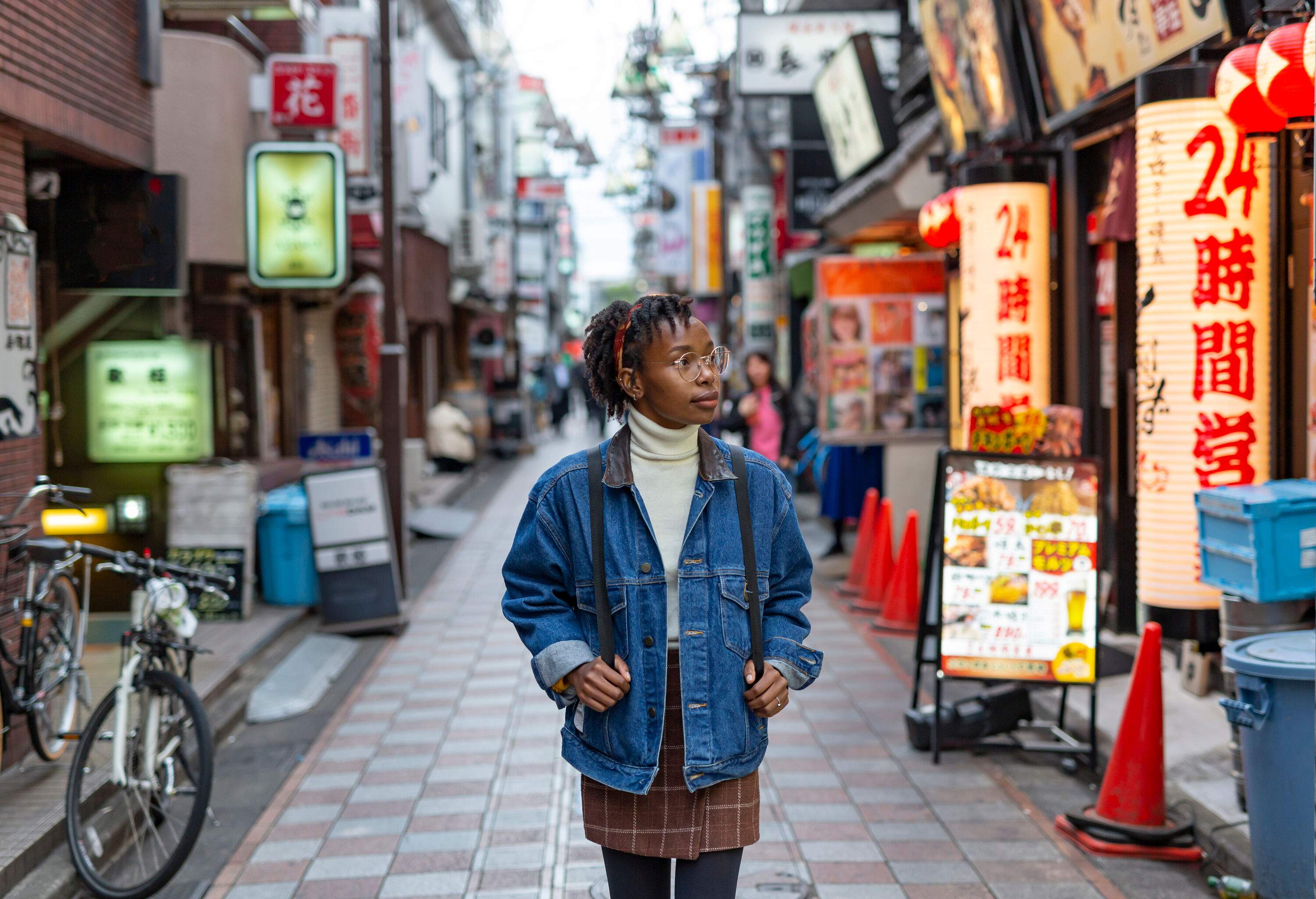 A dark-skinned young female tourist wanders in the street full of various shops, stores, and cafes.