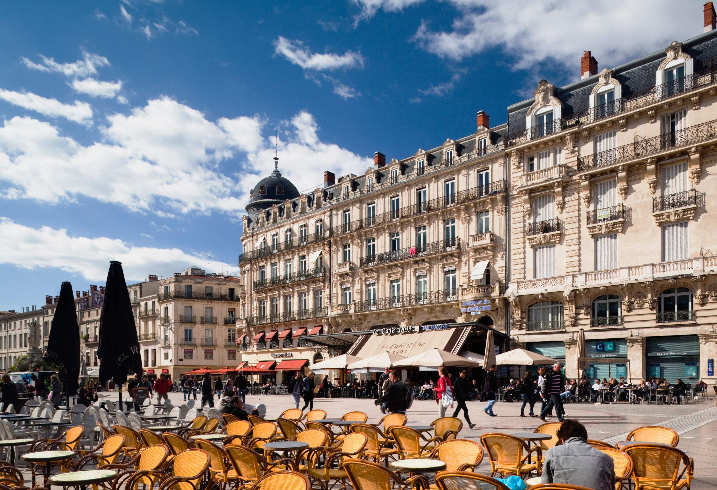 View of an exquisite historical structure from an outdoor café with people walking through the square.