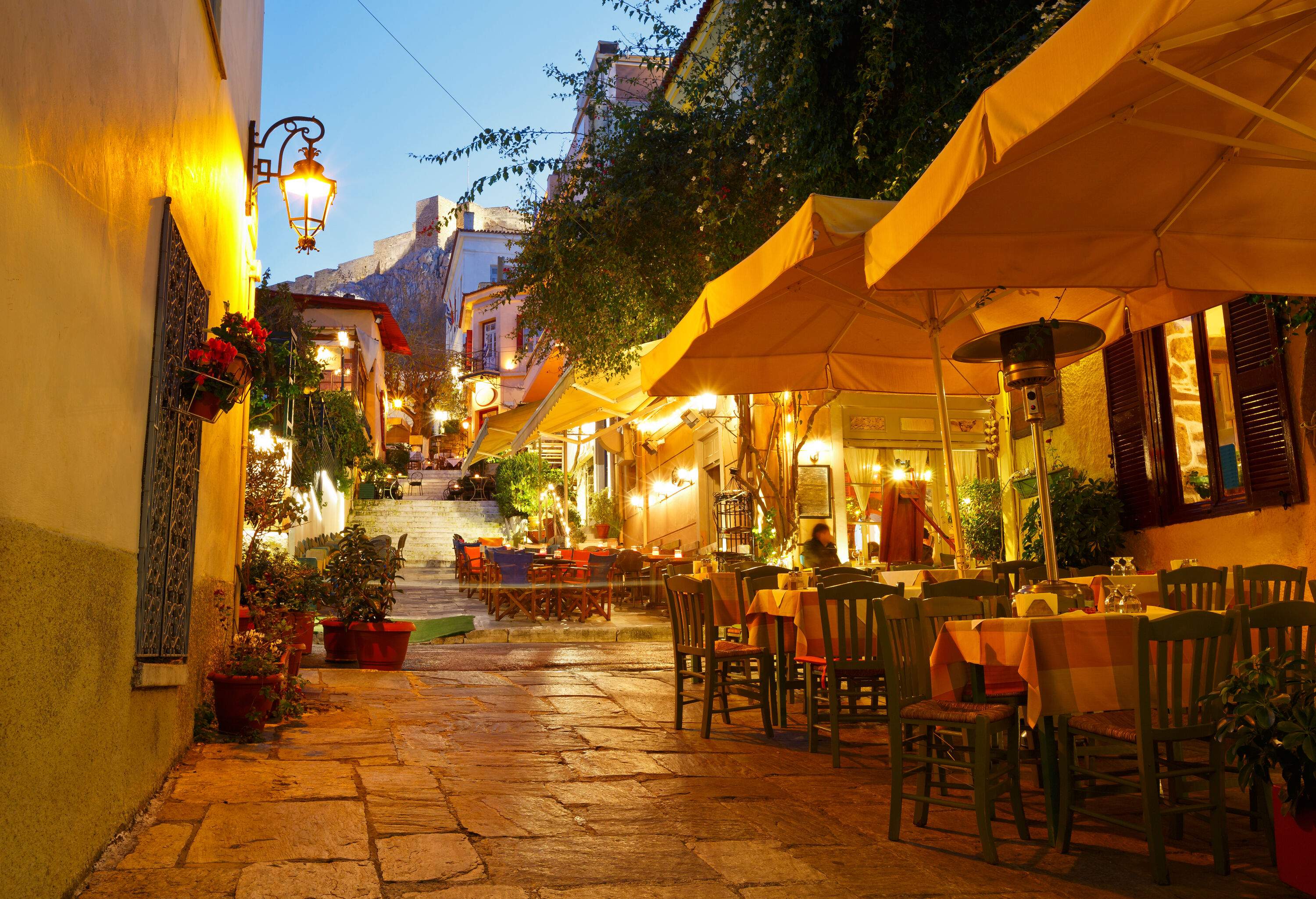 Outdoor cafes lining a narrow alley lit by wall lamps.