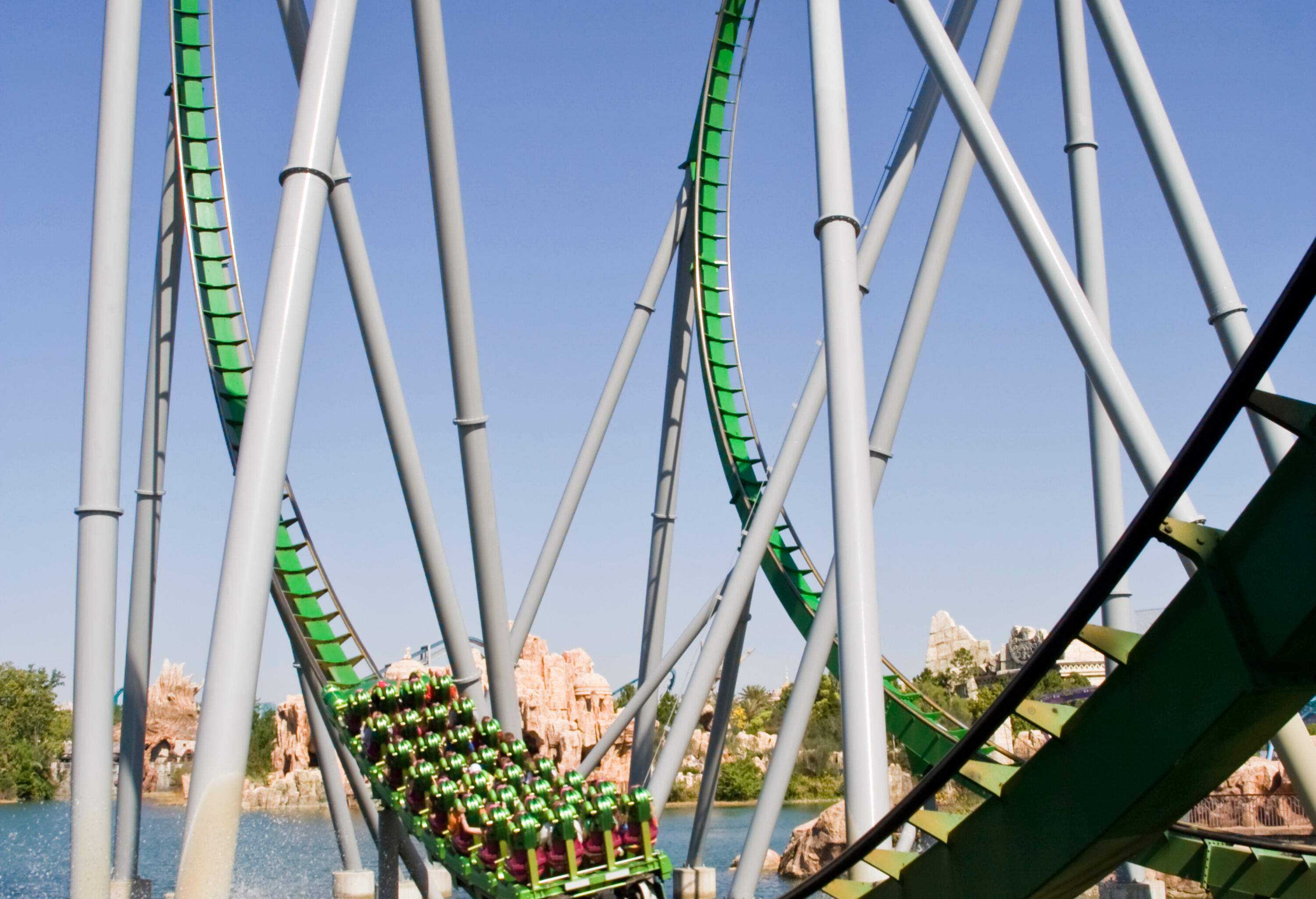 A roller coaster ride descends a twisted track near a pool with water splashes.