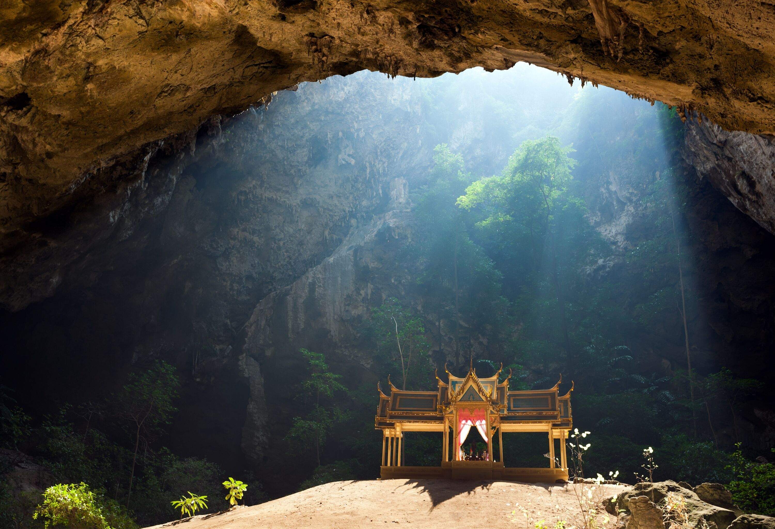 A Buddhist pavilion inside a cave illuminated by sunlight from above.