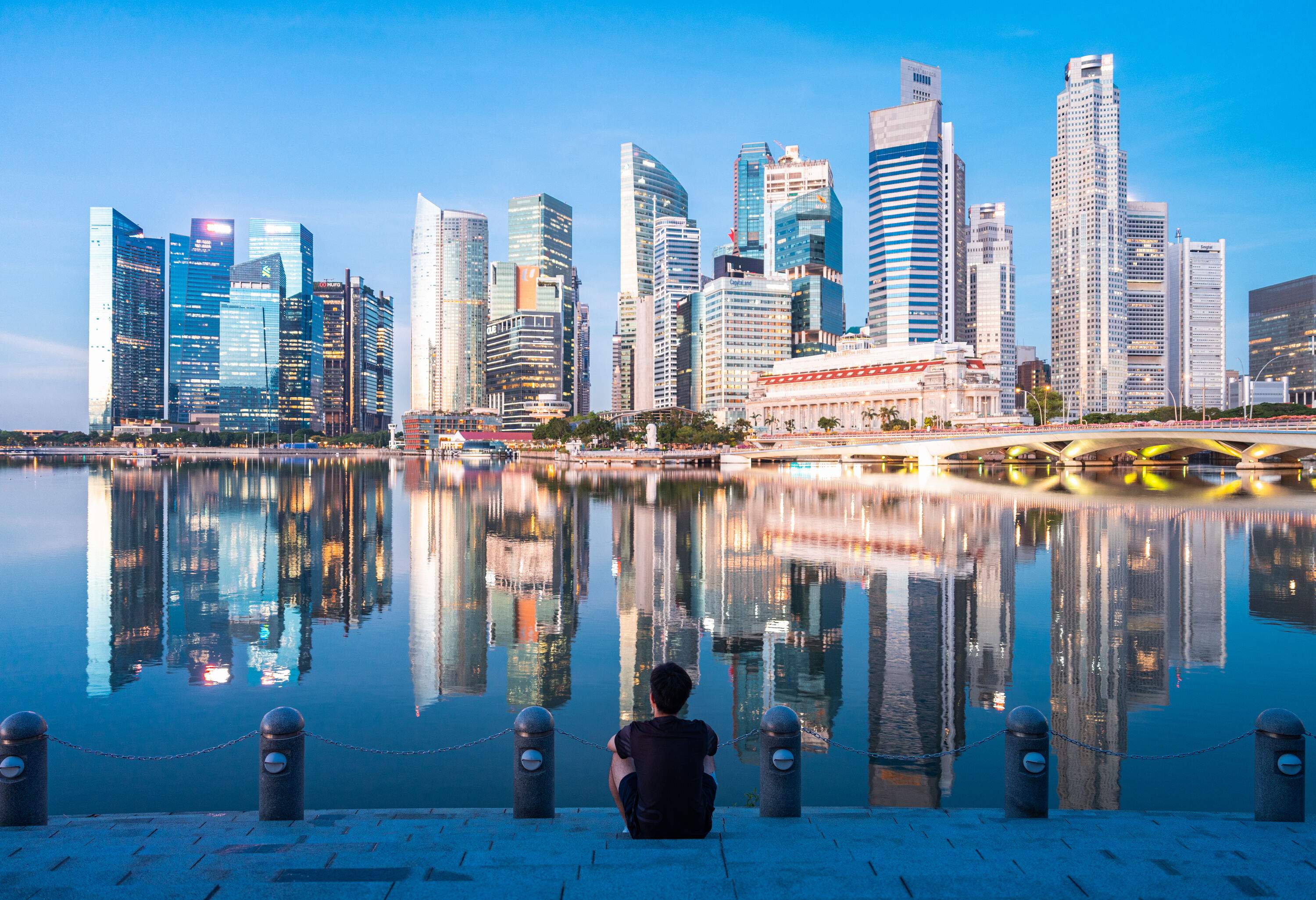 Young man sat on the dock with urban skyline and skyscrapers in Marina Bay Singapore.