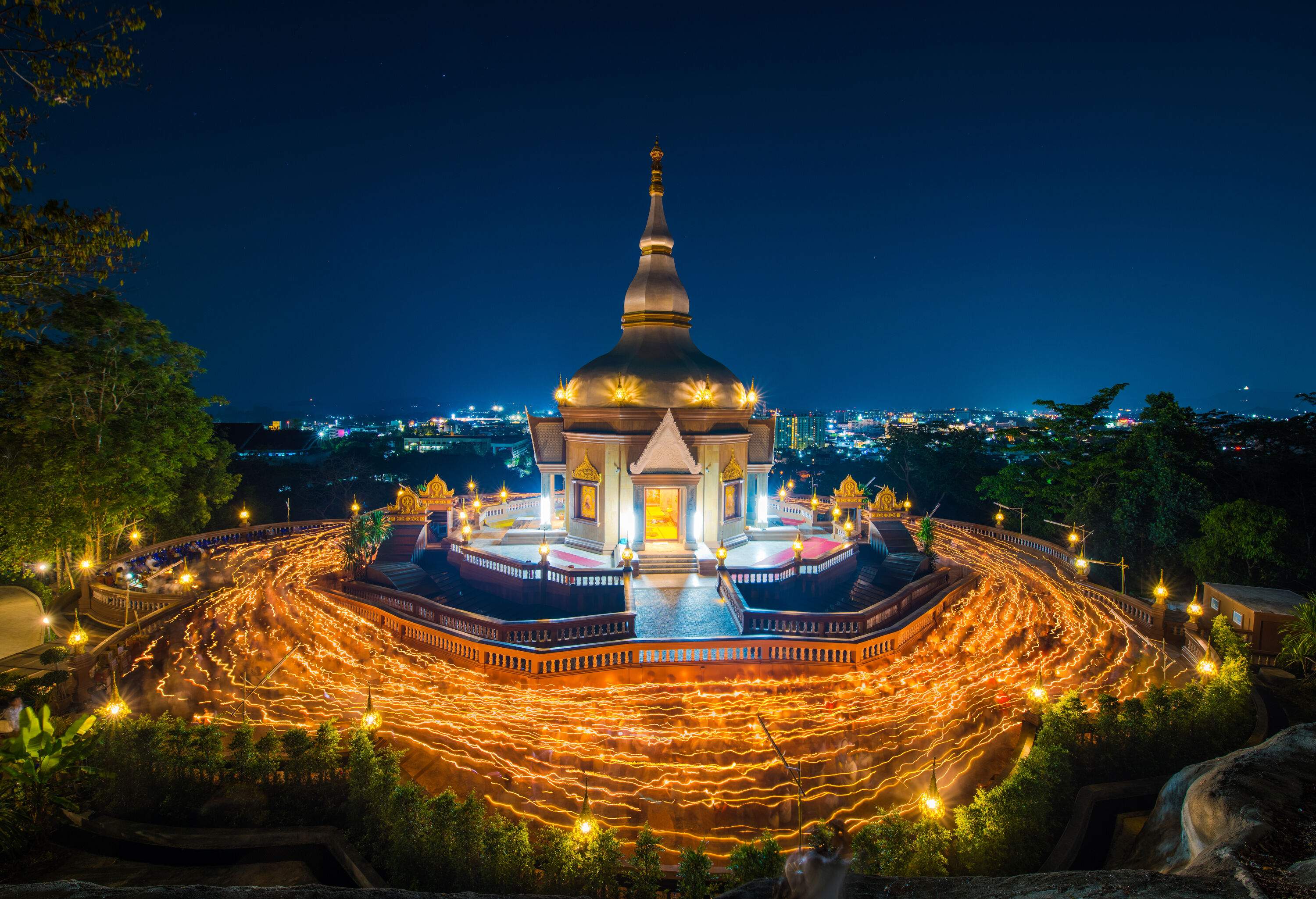 Wat Charoen Samanakij is a temple with a pillared porch and a pointy roof surrounded by streaks of lights at night.