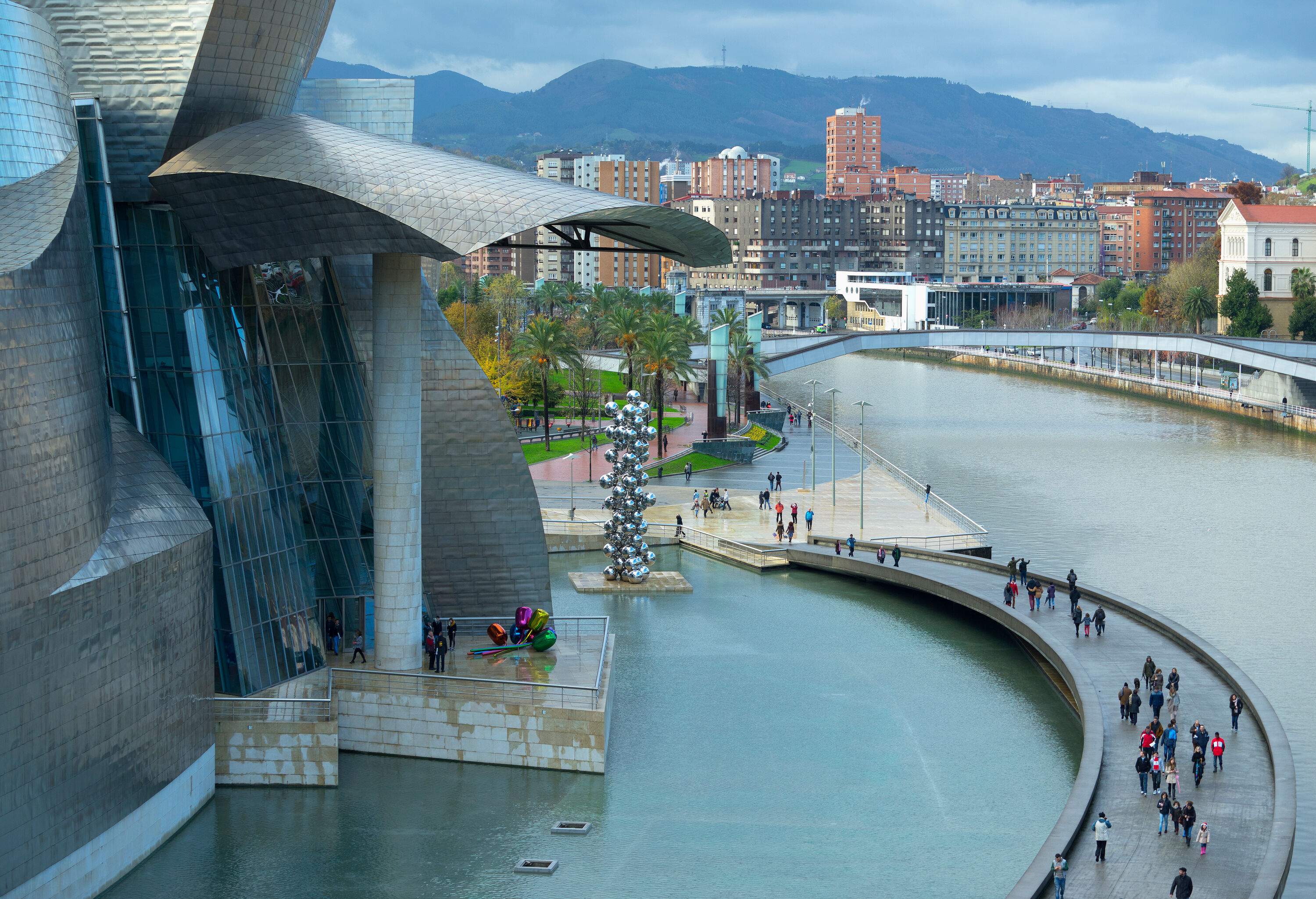 A museum built alongside a river where people pass on a walkway bridge to cross the river to the other side of the building.