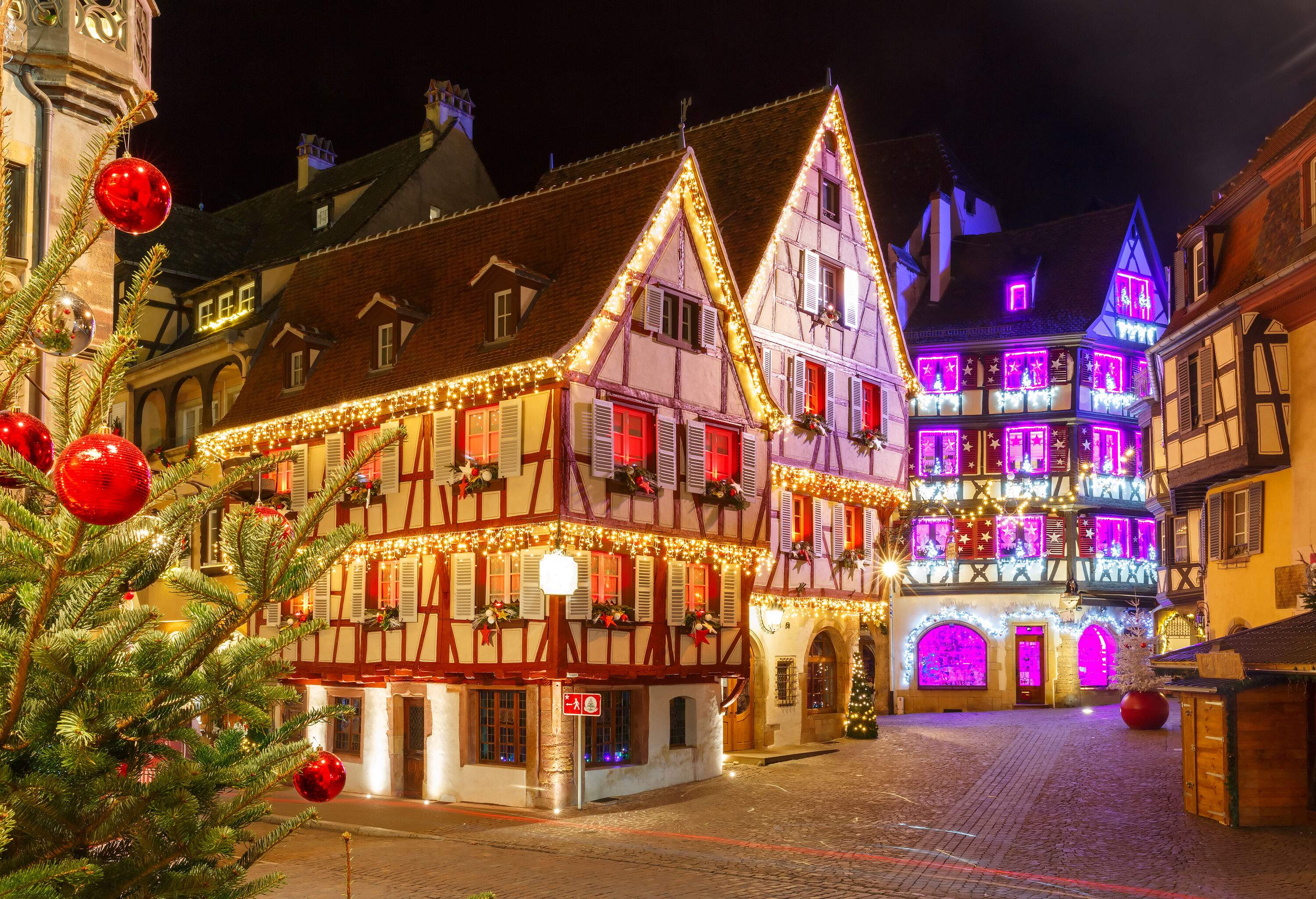Half-timbered houses are brightly illuminated with Christmas lights and decorated with various colourful Christmas ornaments.