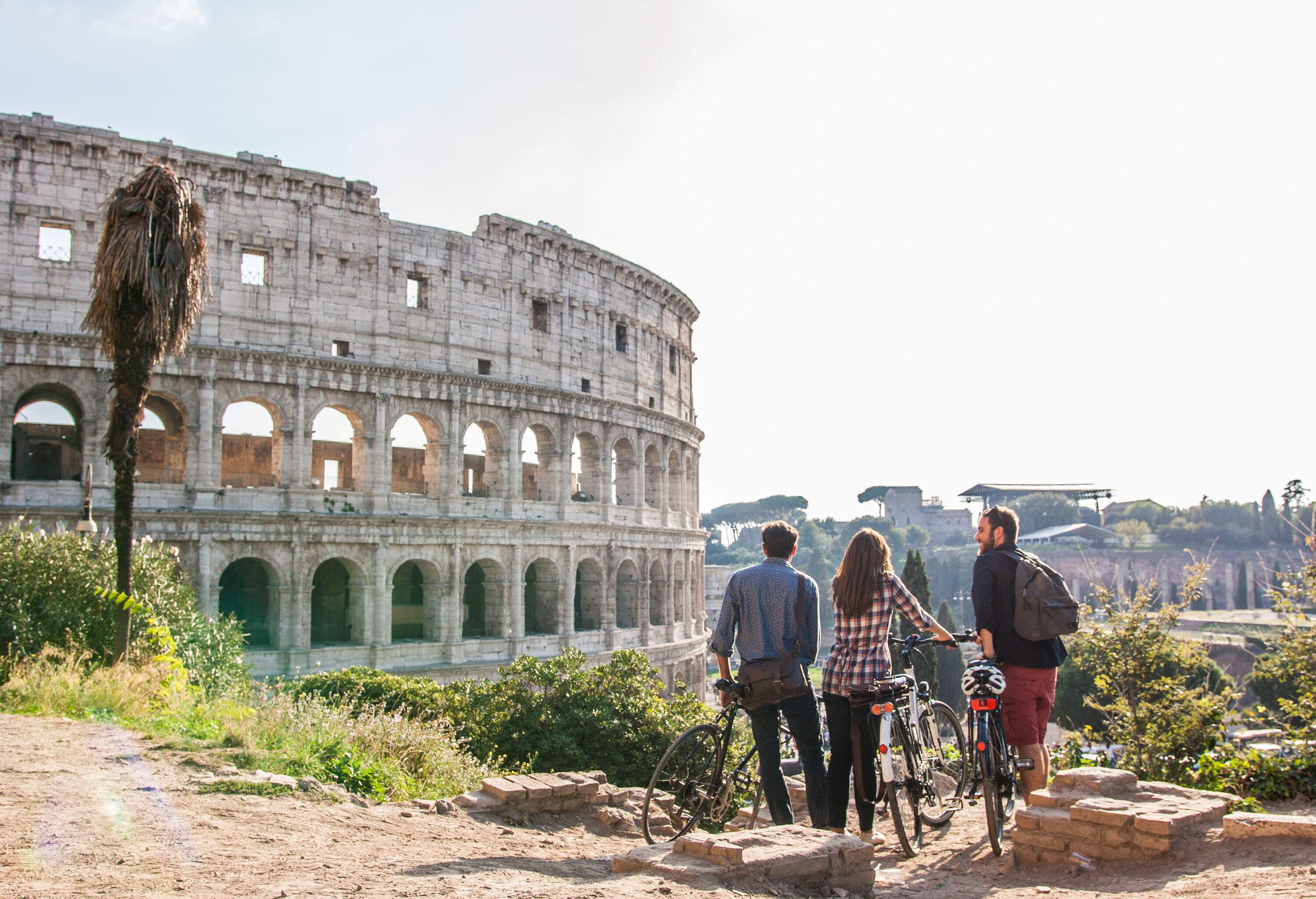 Three friends with bikes standing on a ledge with views of the famous Colosseum.