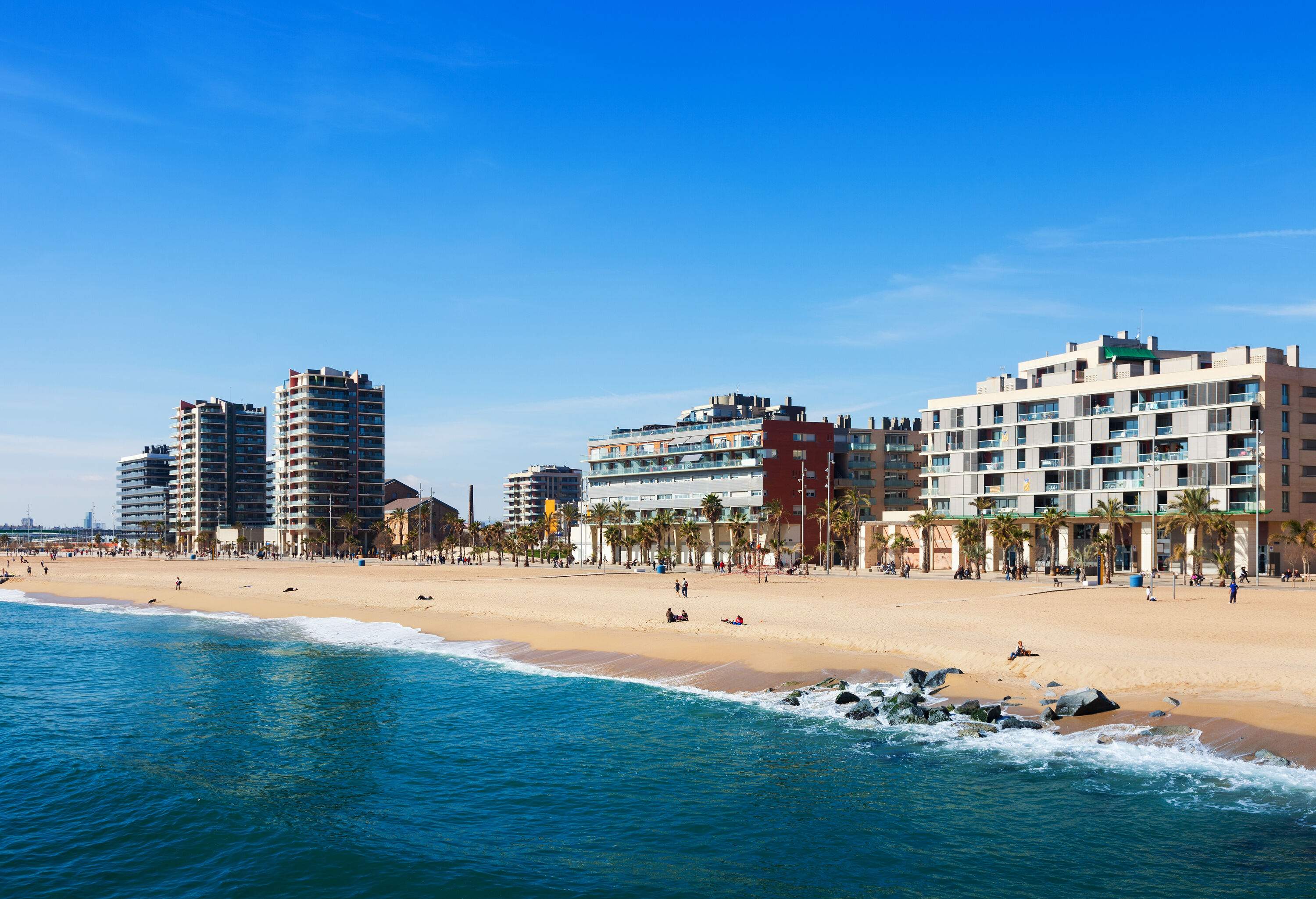 Turquoise beach water, people on the beach shore, and resort buildings in the background.