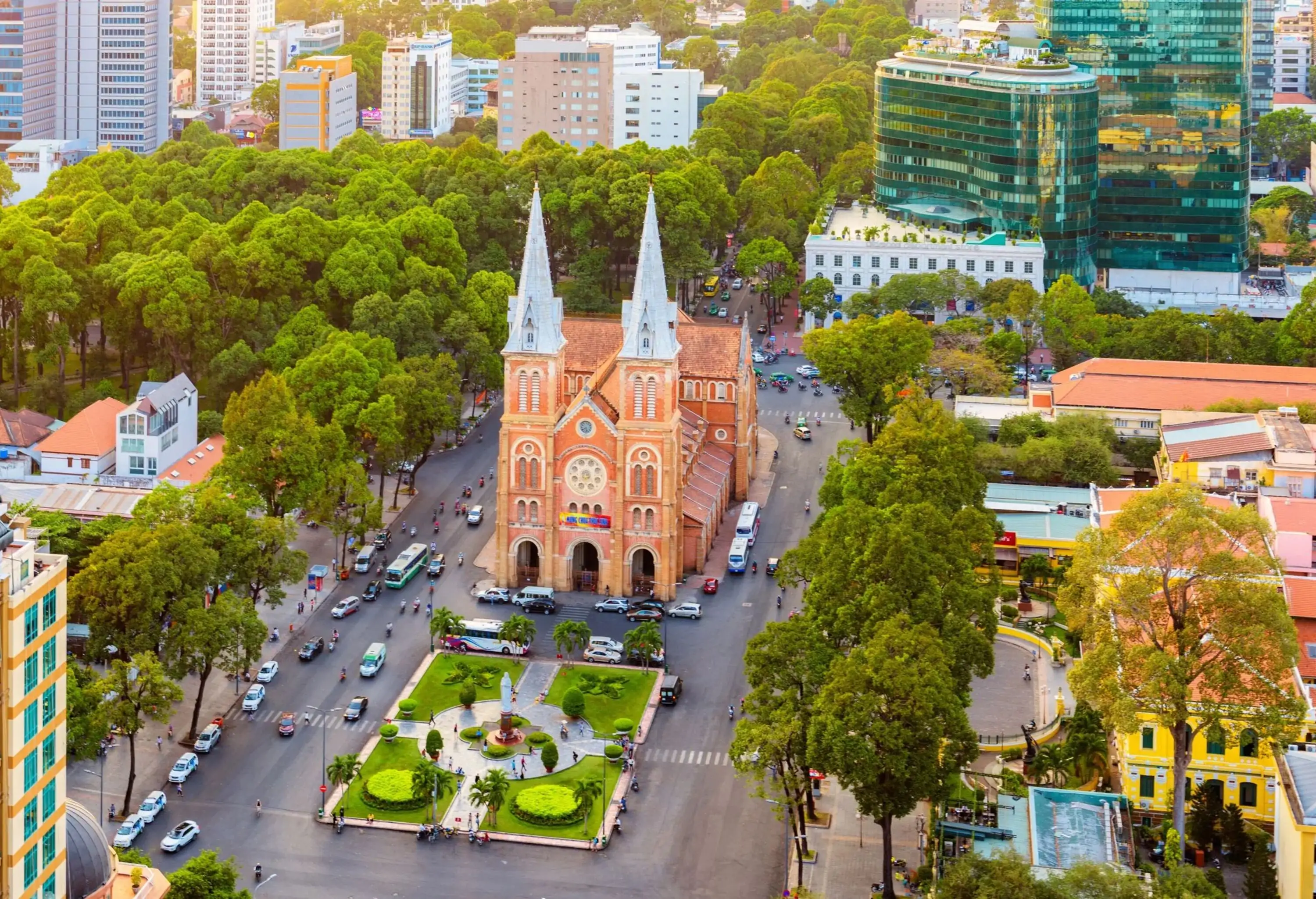 Aerial view of an old city with a mixture of classic and modern structures with a magnificent Catholic cathedral constructed with elegant French bricks, showcasing two impressive Romanesque bell towers, stands as a centrepiece enveloped by lush foliage.