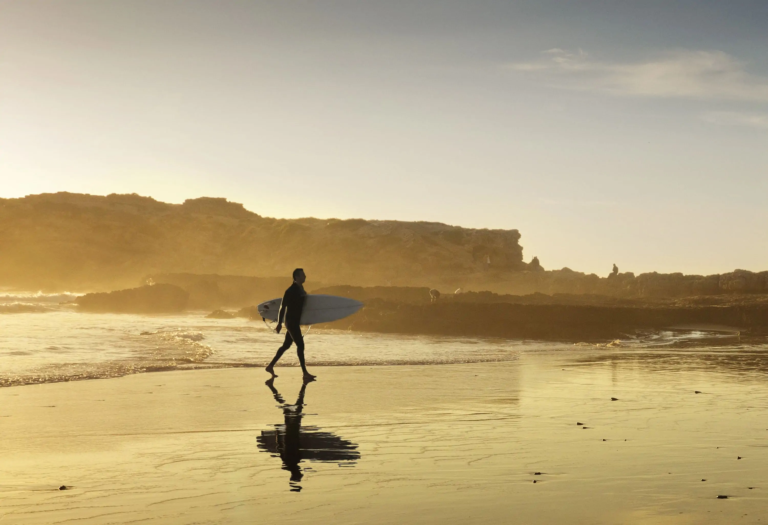 A man carrying a surfboard as he walks across the beach towards the coast.